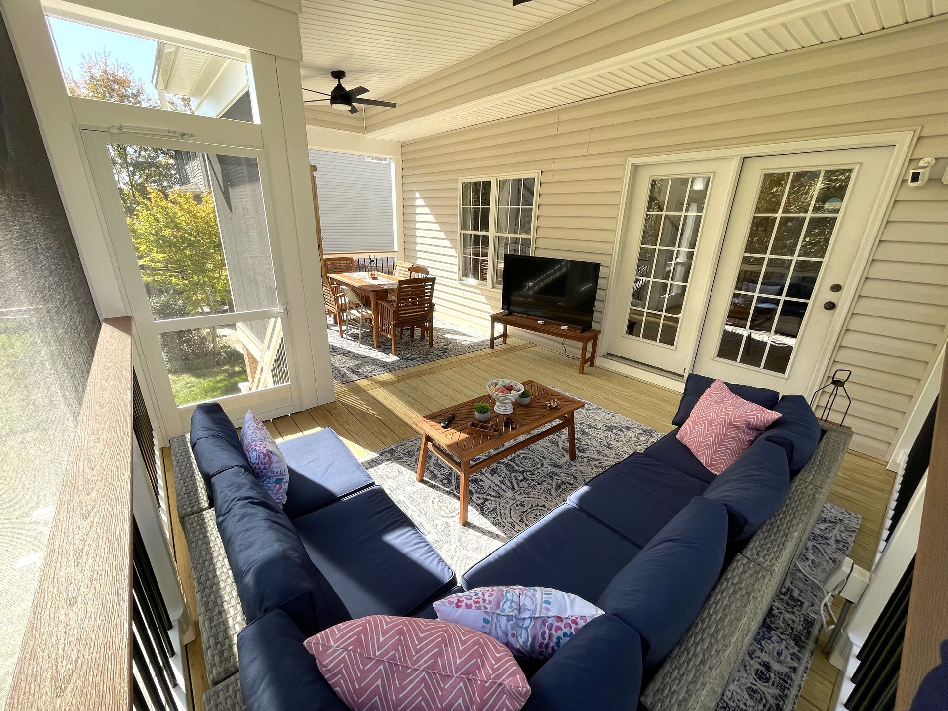 Covered porch with navy sectional, wooden coffee table, dining set, and fireplace by French doors.
