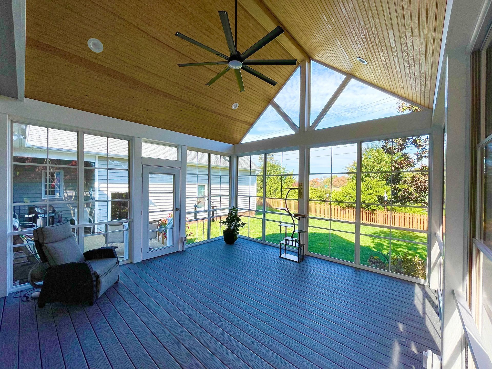 Covered patio with blue flooring, vaulted wood ceiling, and large windows overlooking a backyard garden.