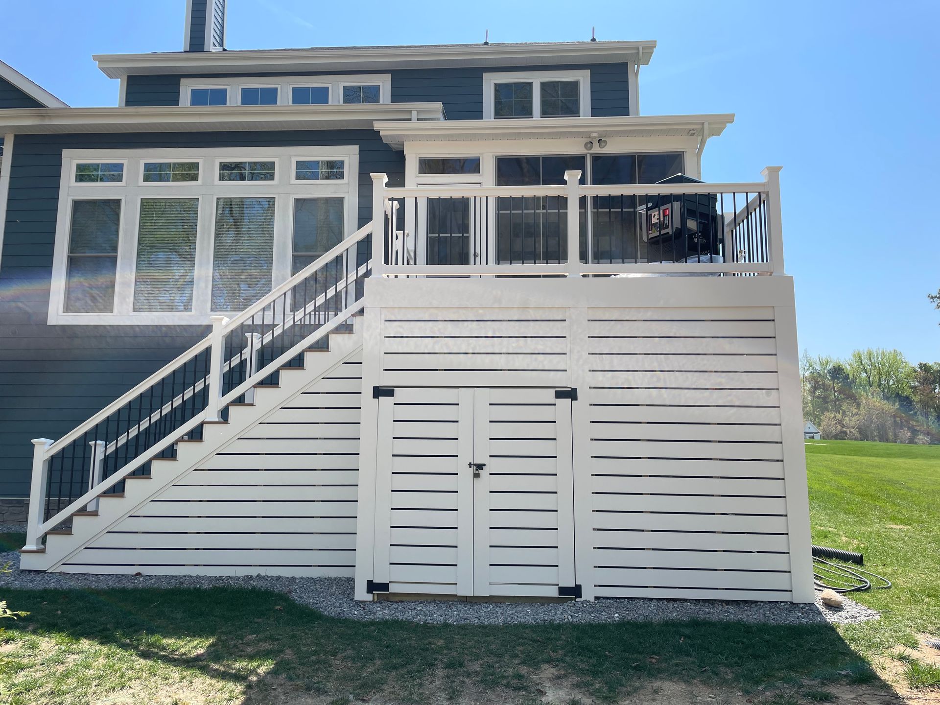 Modern two-story house with white deck stairs and screened porch under a clear blue sky