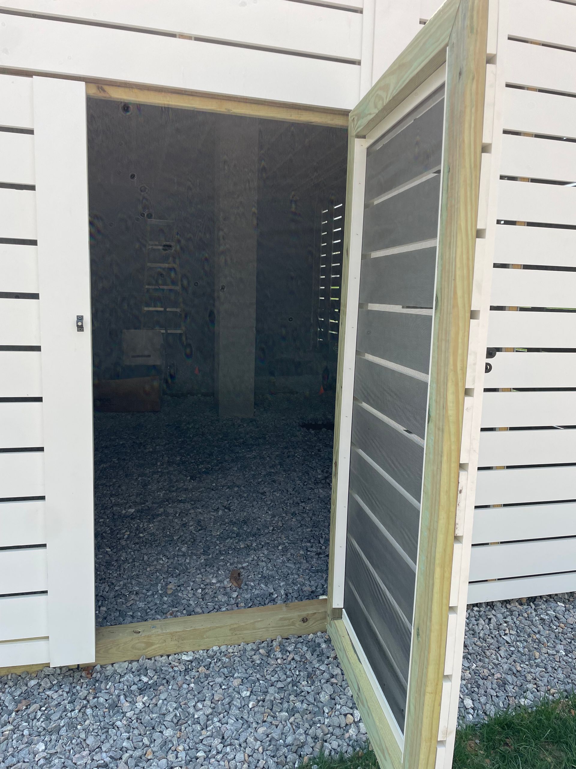 Open exterior door with screen door, revealing a dark interior and gravel path outside.