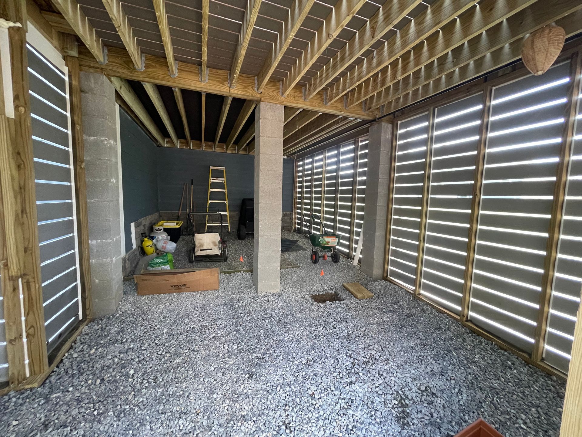 Interior of unfinished shed with gravel floor, exposed wooden framing, and construction materials stacked inside