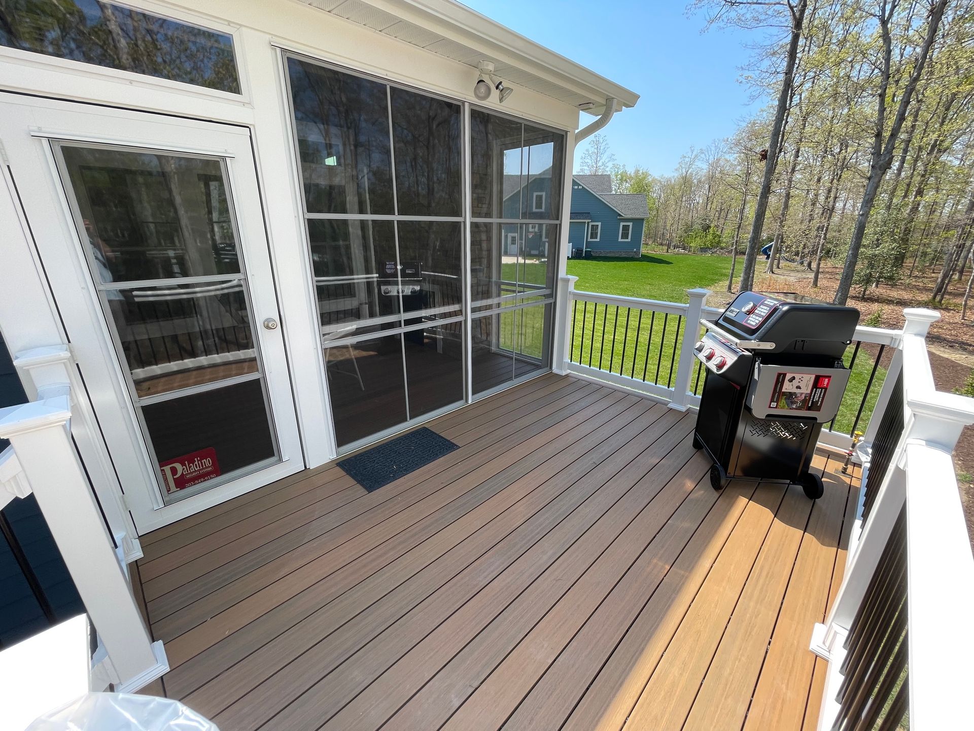 Screened porch with tan decking, white railing, and a black grill beside sliding glass doors.