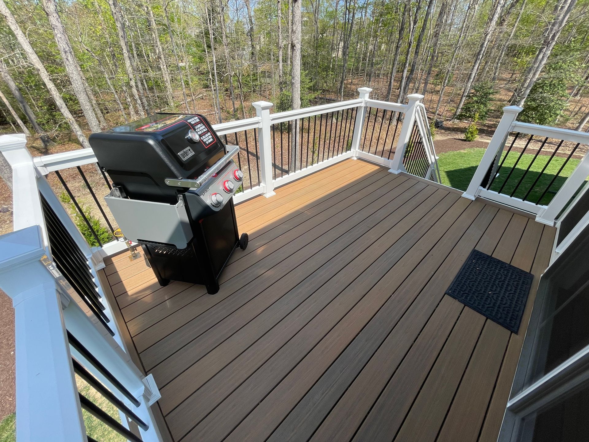 Deck with black grill and railing, overlooking a wooded yard
