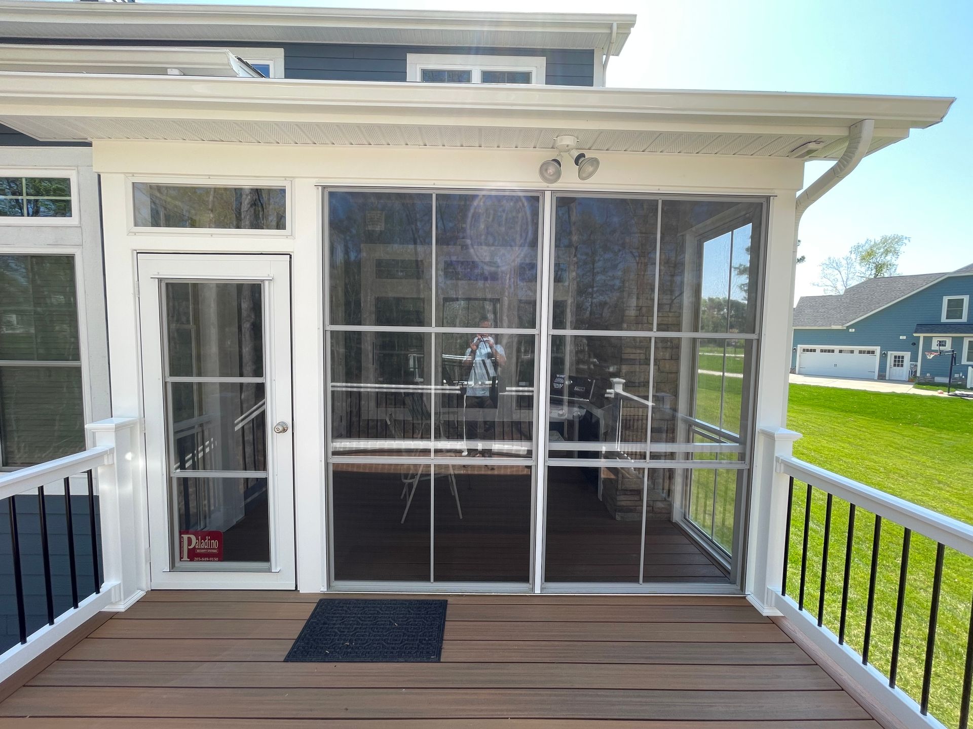 Covered porch with white door and large windows overlooking a grassy yard.