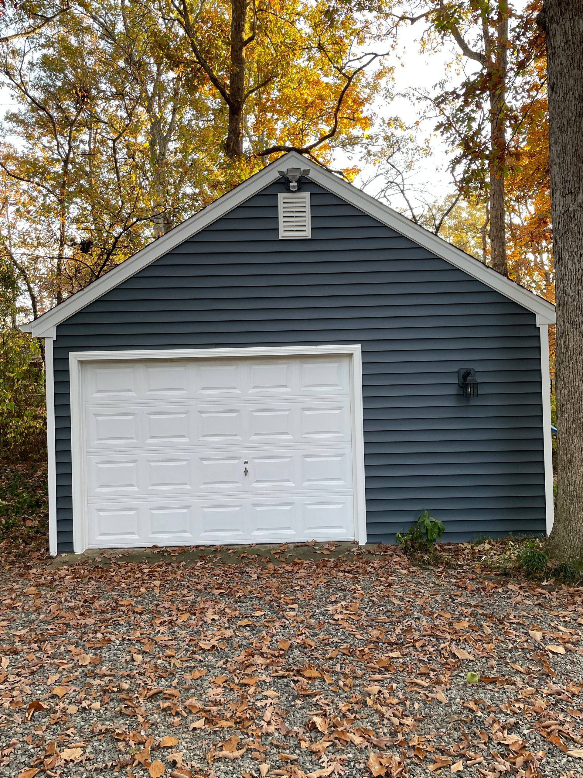Gray detached garage with white door, set among autumn trees and fallen leaves