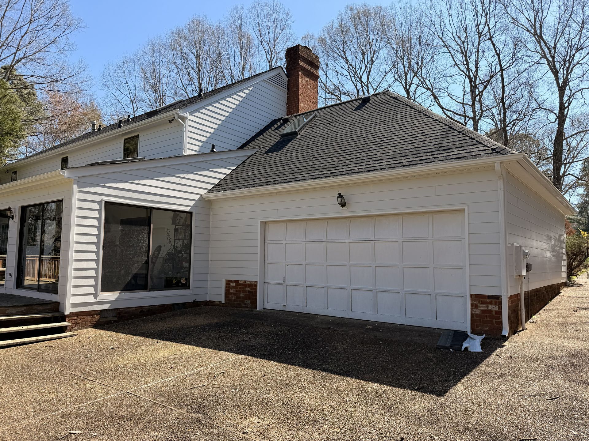 Suburban house with white siding, a two-car garage, and leafless trees on a sunny day