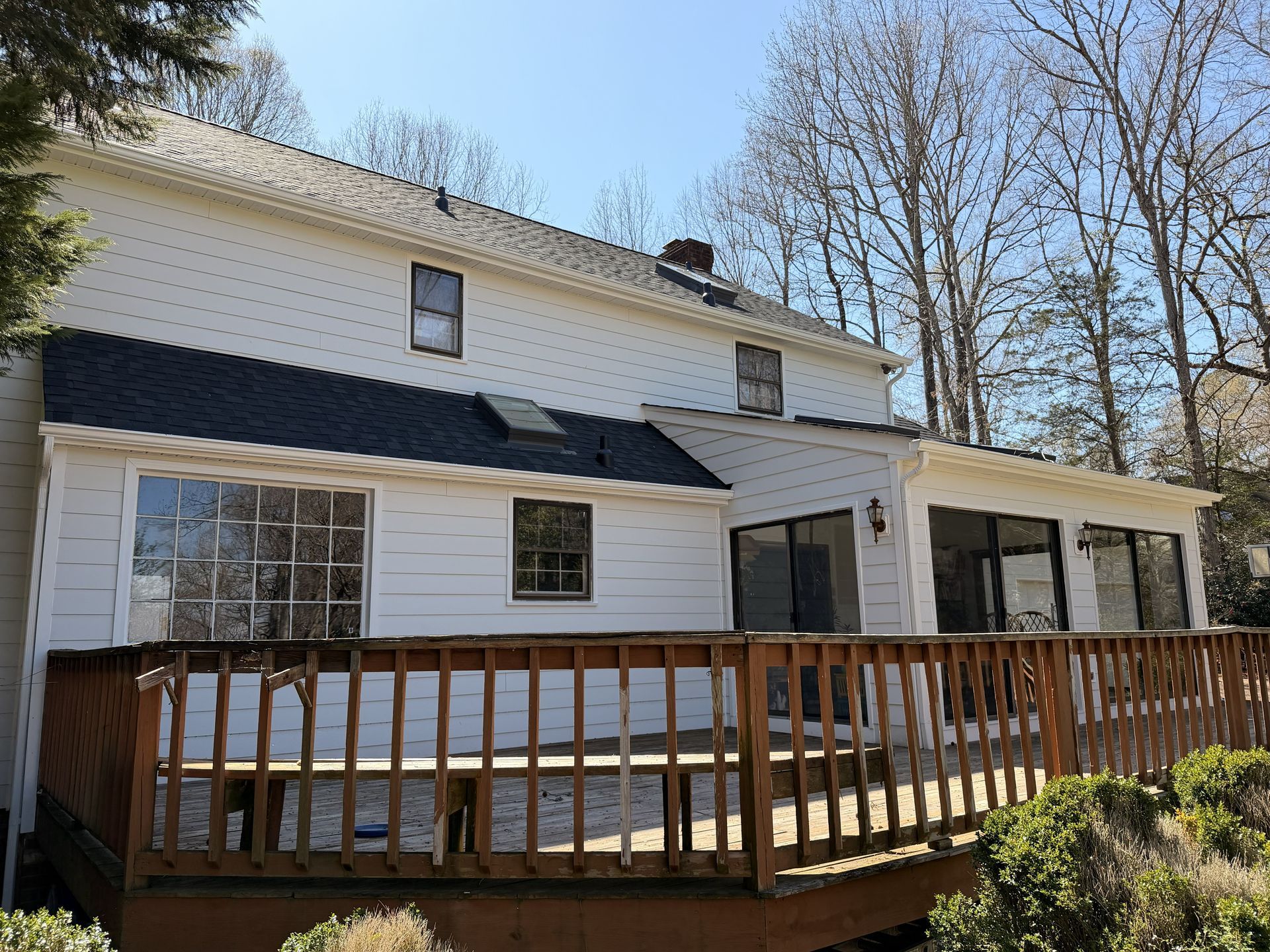 Back deck with wooden railing on a white two-story house under a clear blue sky