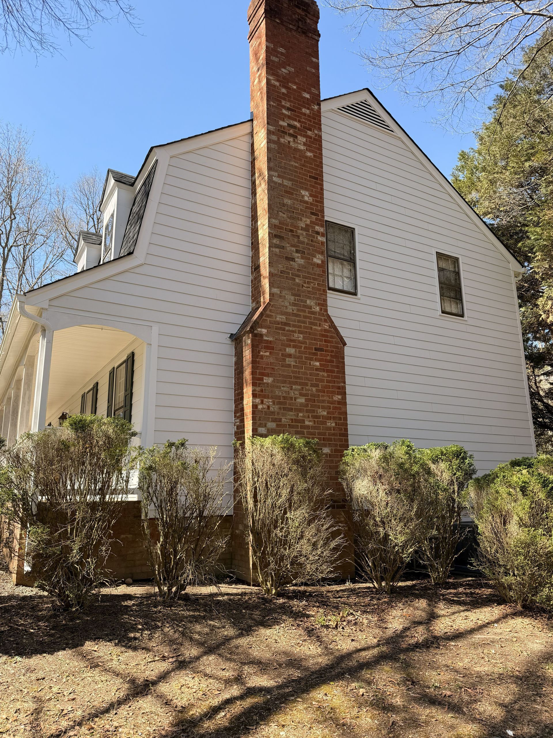 White house with red brick chimney, surrounded by shrubs and trees on a sunny day