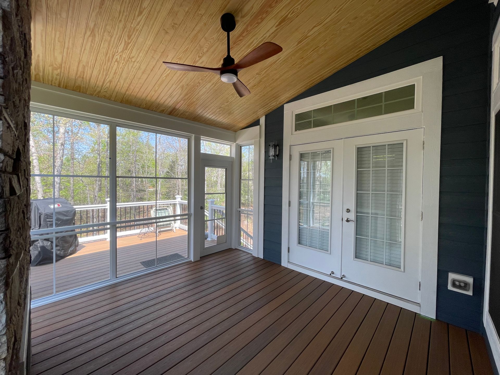 Covered porch with wood ceiling, ceiling fan, white French doors, and screened windows overlooking a driveway.