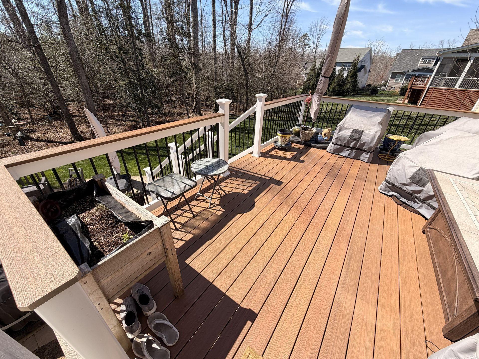 Wooden backyard deck with railing, lounge chairs, and a grill in sunny daylight