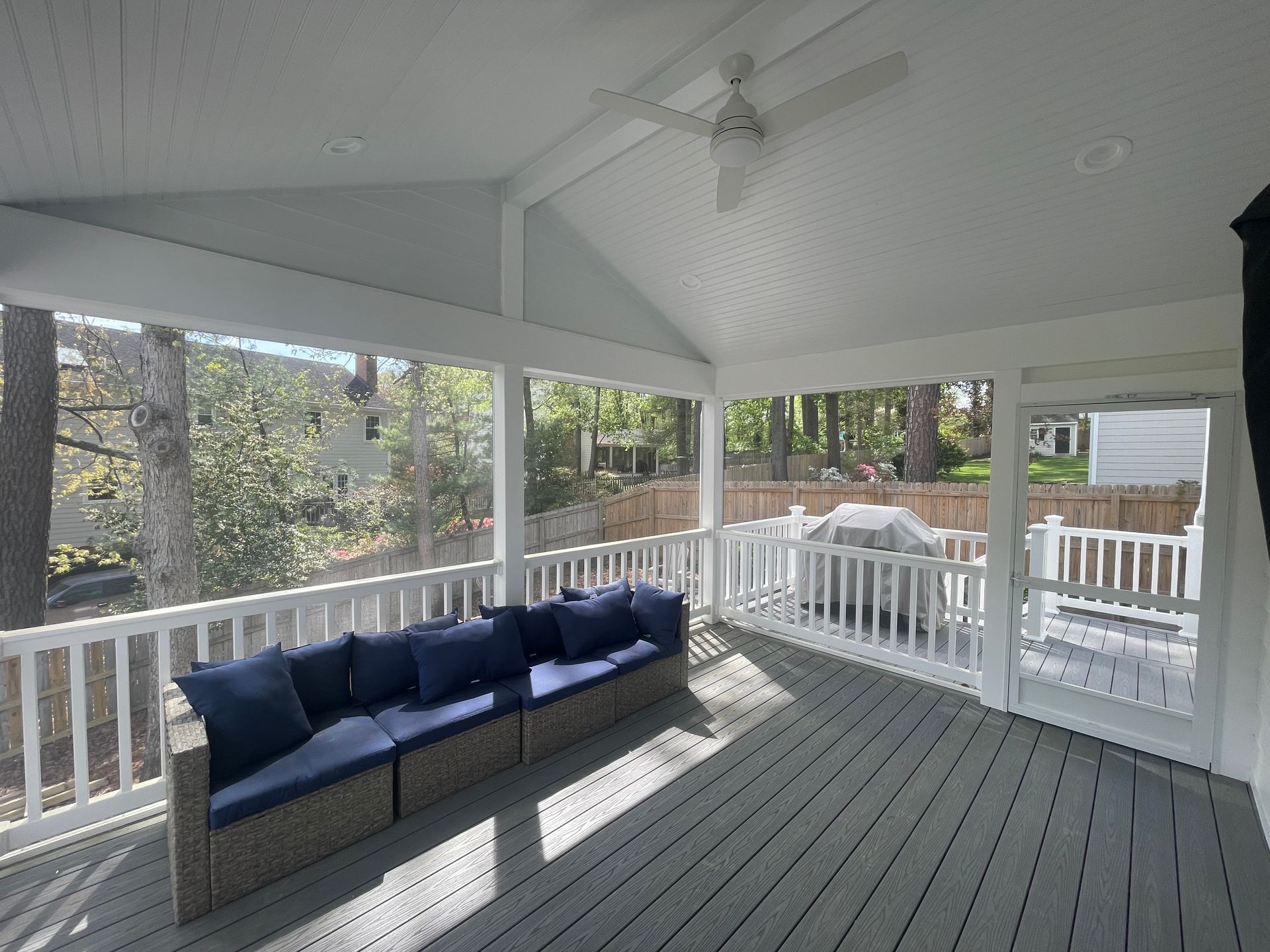 Covered porch with white railings, gray floor, and a navy blue cushioned sofa.