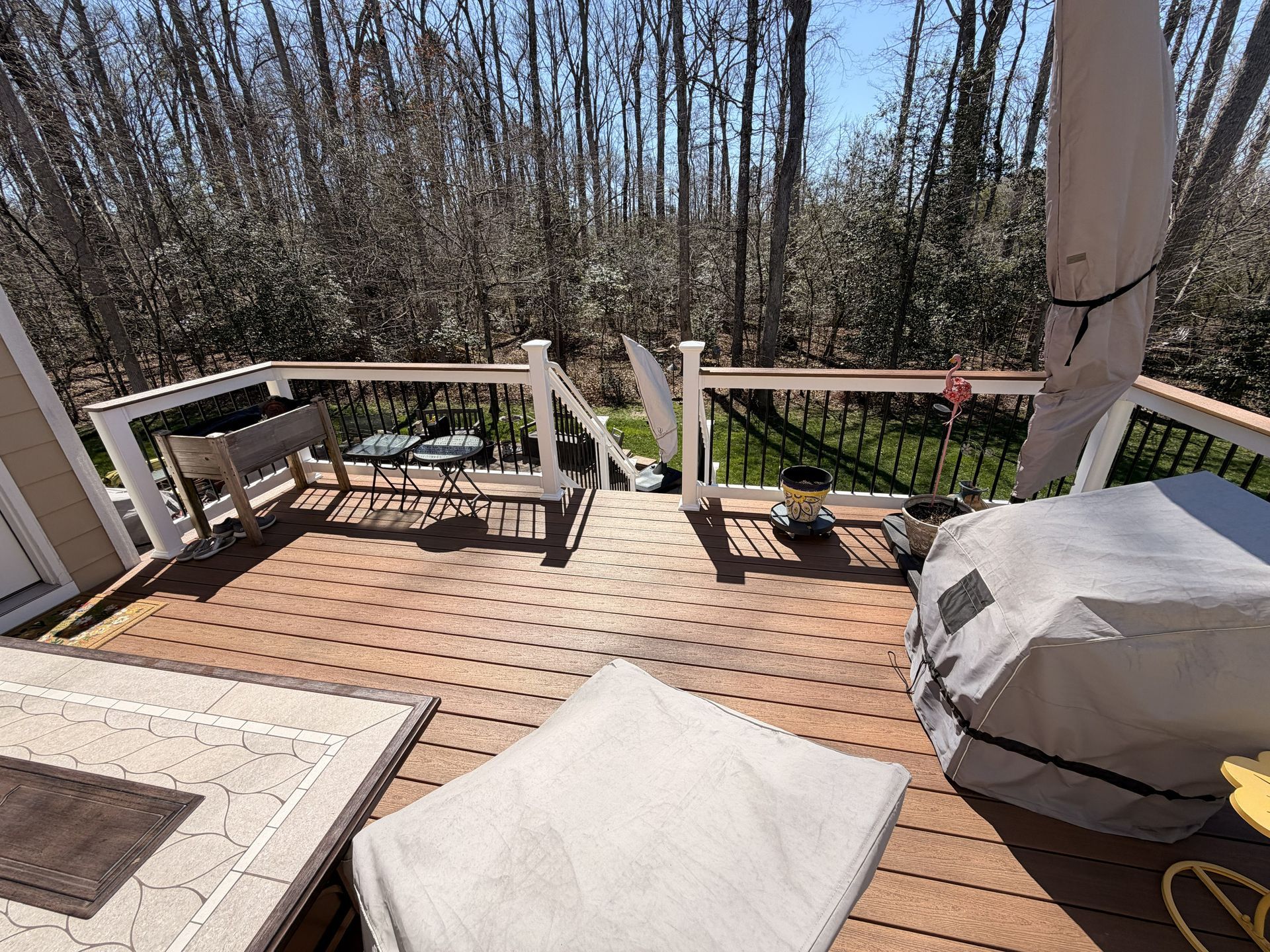 Wooden deck with outdoor furniture and a grill, overlooking leafless trees on a sunny day