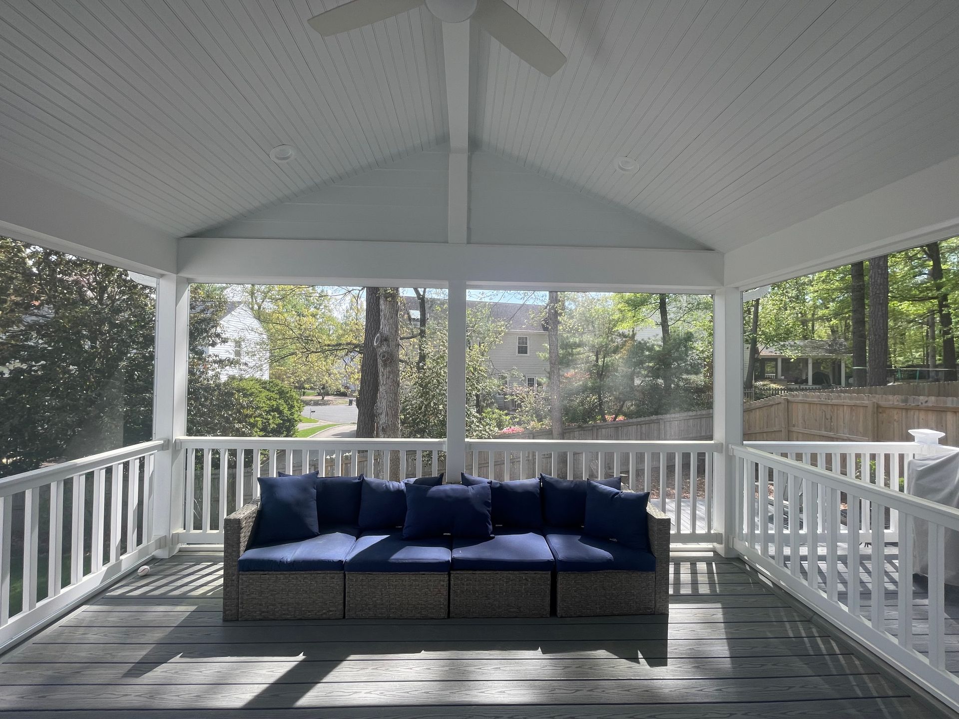 Covered porch with white railings and a dark blue outdoor sofa overlooking a wooded yard