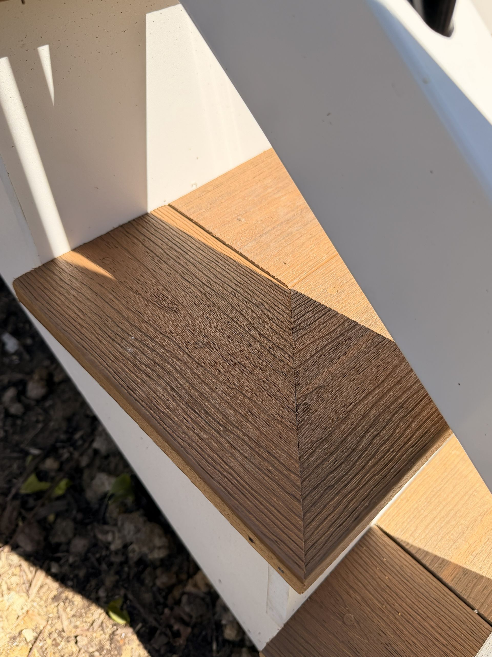Close-up of a textured brown wooden step on a white railing, lit by sunlight and shadow.