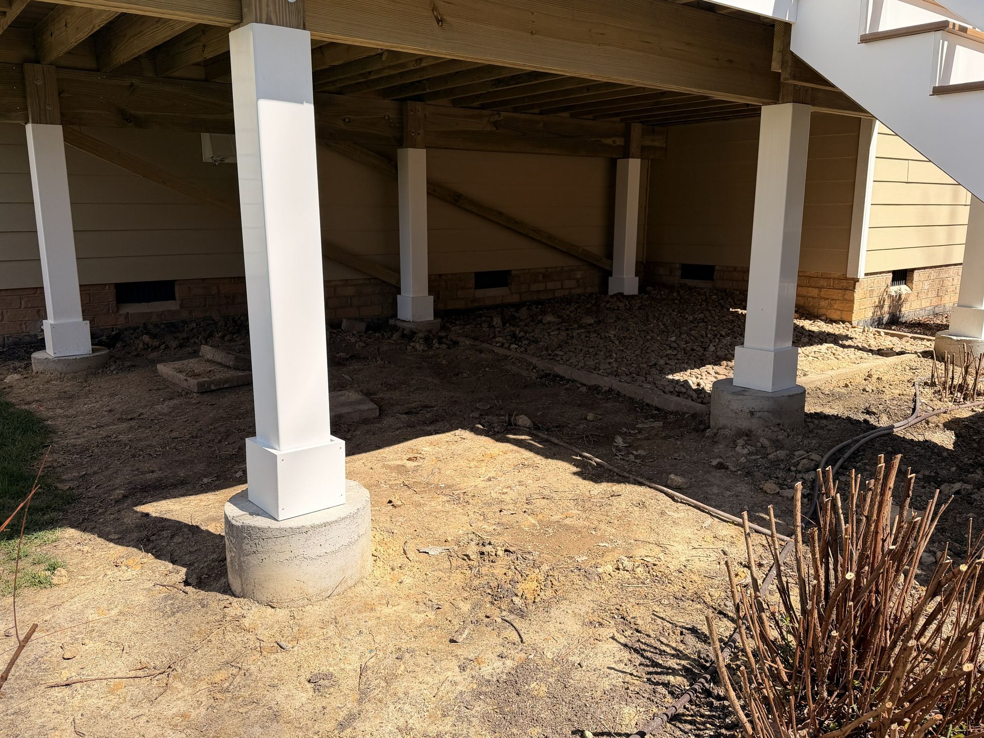 Raised house undercarriage with white support posts on concrete footings and dry ground beneath.