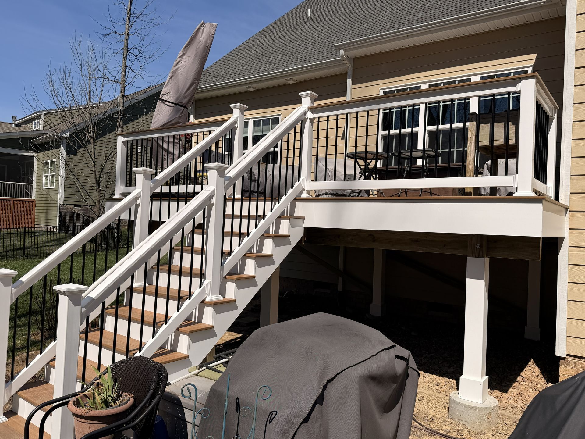 Backyard deck with white railing, stairs, and a covered grill beside a brick house