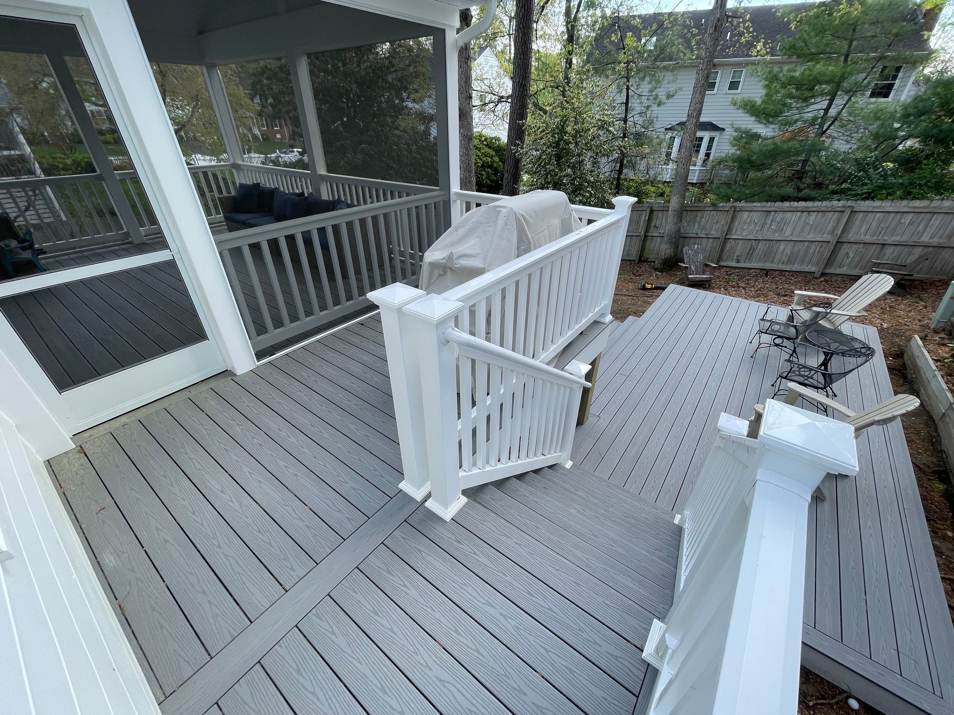 White deck with railings and a covered porch, featuring a gray outdoor grill or fire pit in a residential backyard.