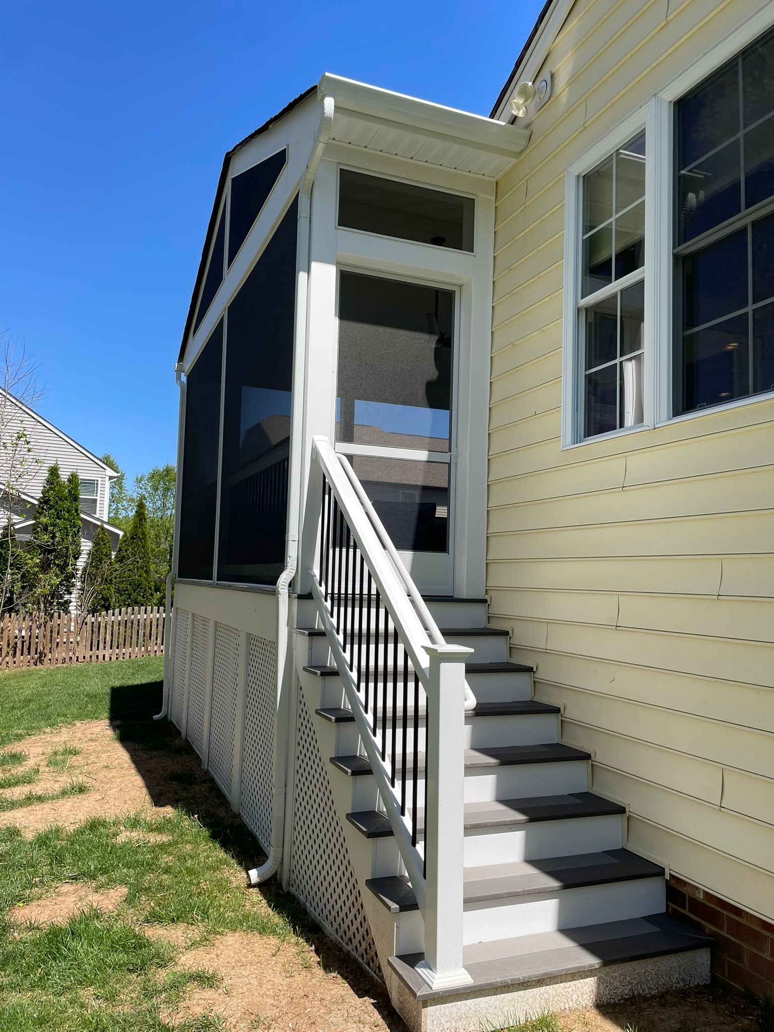 Side entrance stairs with white railing leading to a beige house with black screened porch.