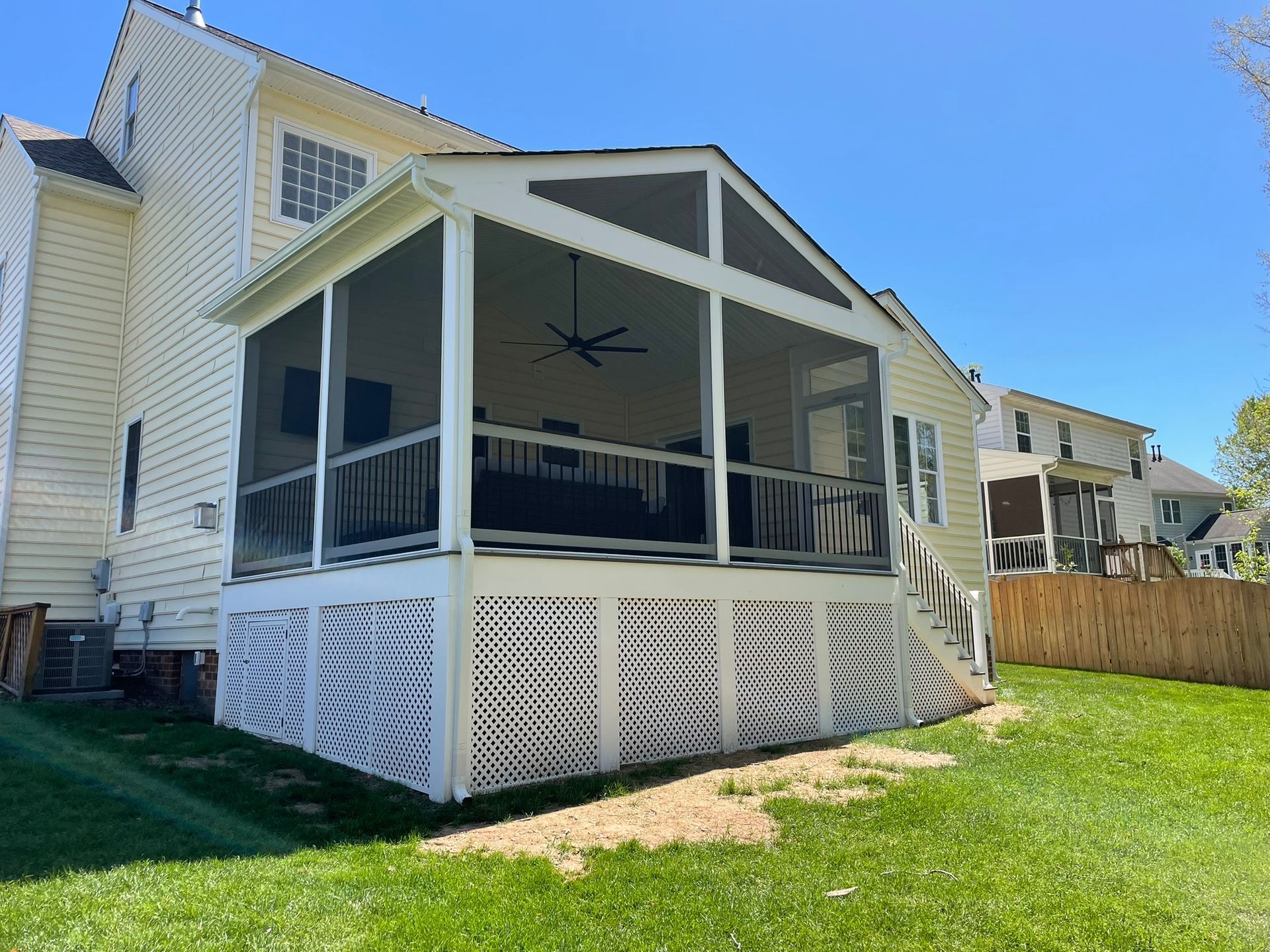 White house with a screened back porch and lattice skirting in a grassy backyard under a blue sky