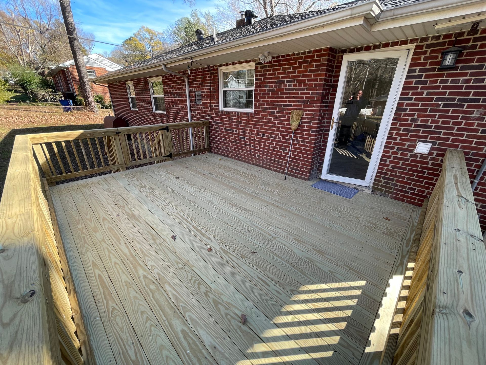 Wooden backyard deck attached to a red brick house with a glass door and railing.