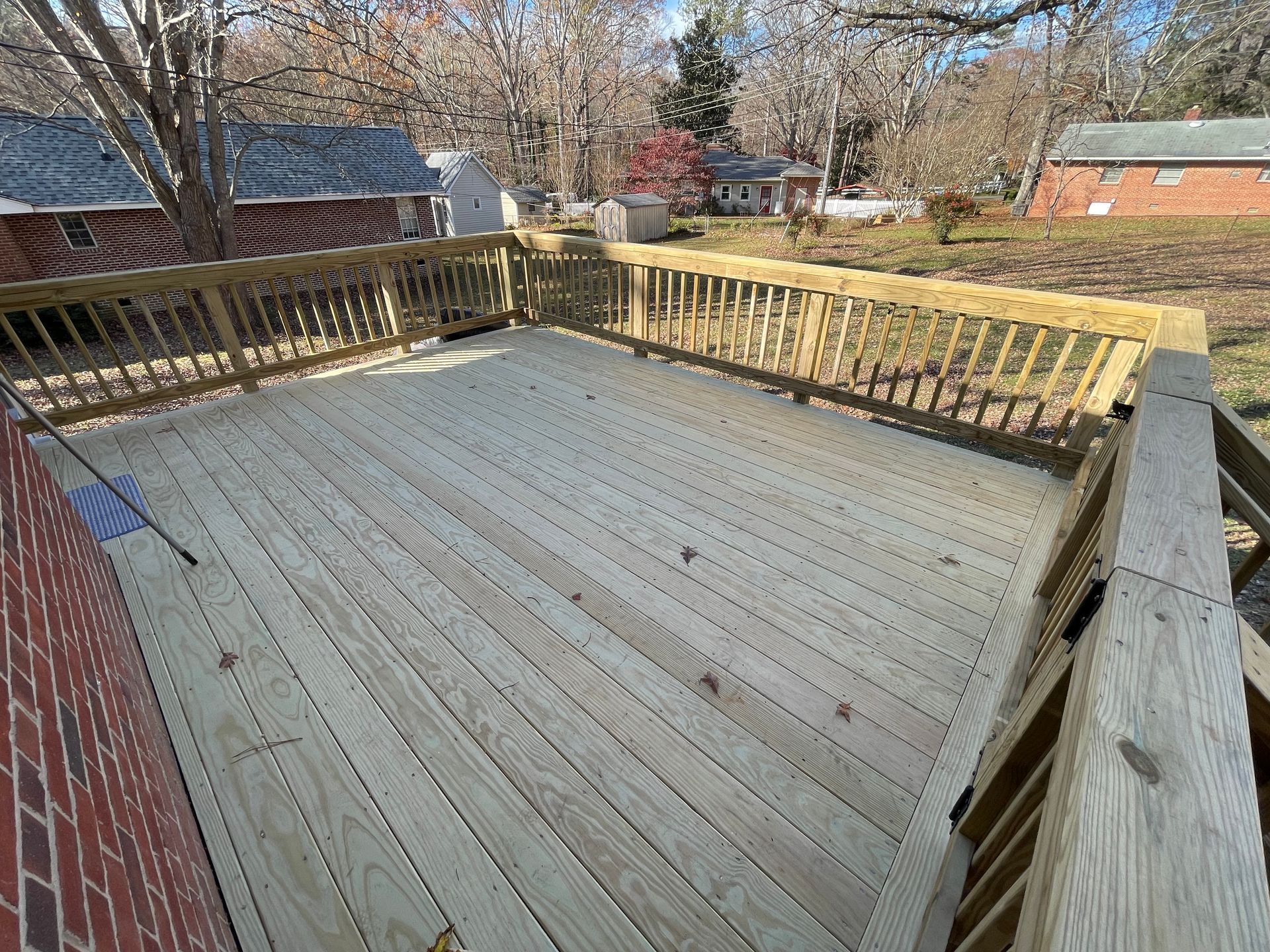 Wooden backyard deck with railings beside a brick house, viewed on a sunny day