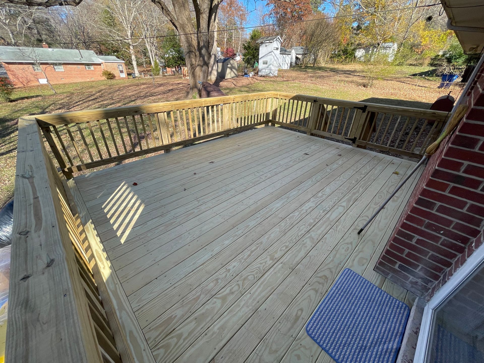 Wooden backyard deck with railing beside a brick house, overlooking a yard and trees