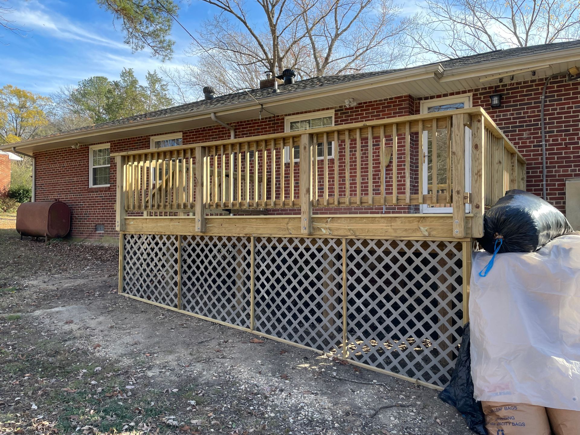 Wooden deck with railing attached to a brick house, with lattice skirting underneath and a grill nearby