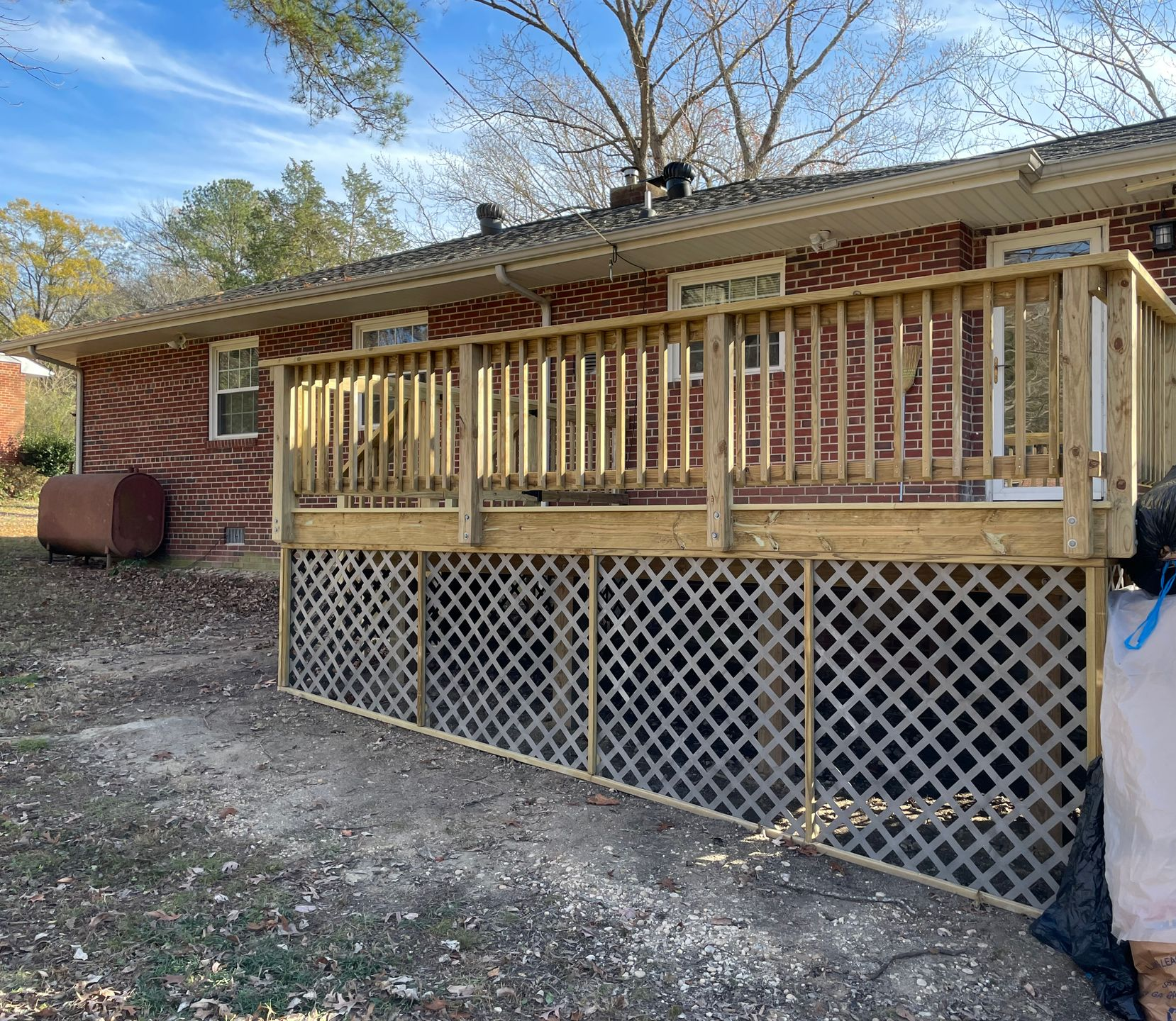 Wooden porch deck with railings and lattice skirting attached to a brick house