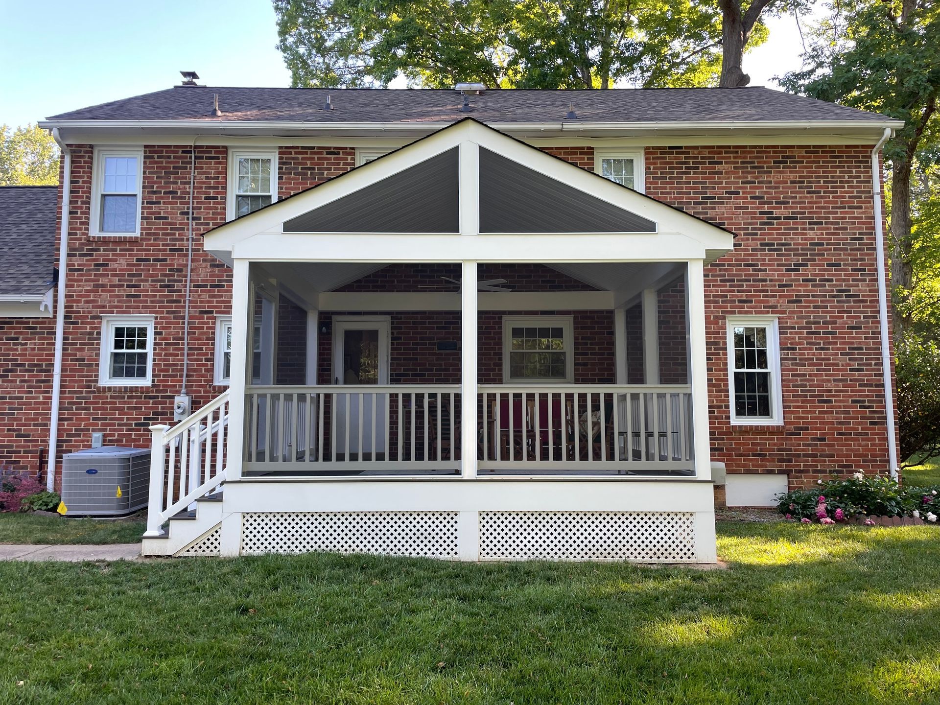 Brick house with a white porch and green lawn, centered under trees.