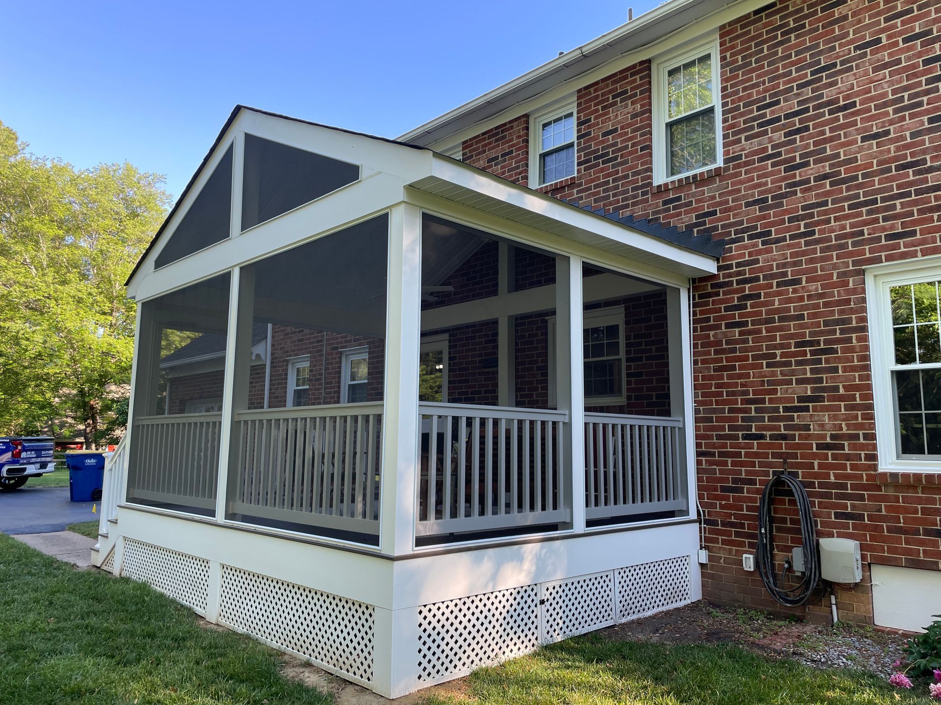 Screened front porch attached to a brick house, with white railings and lattice skirting.