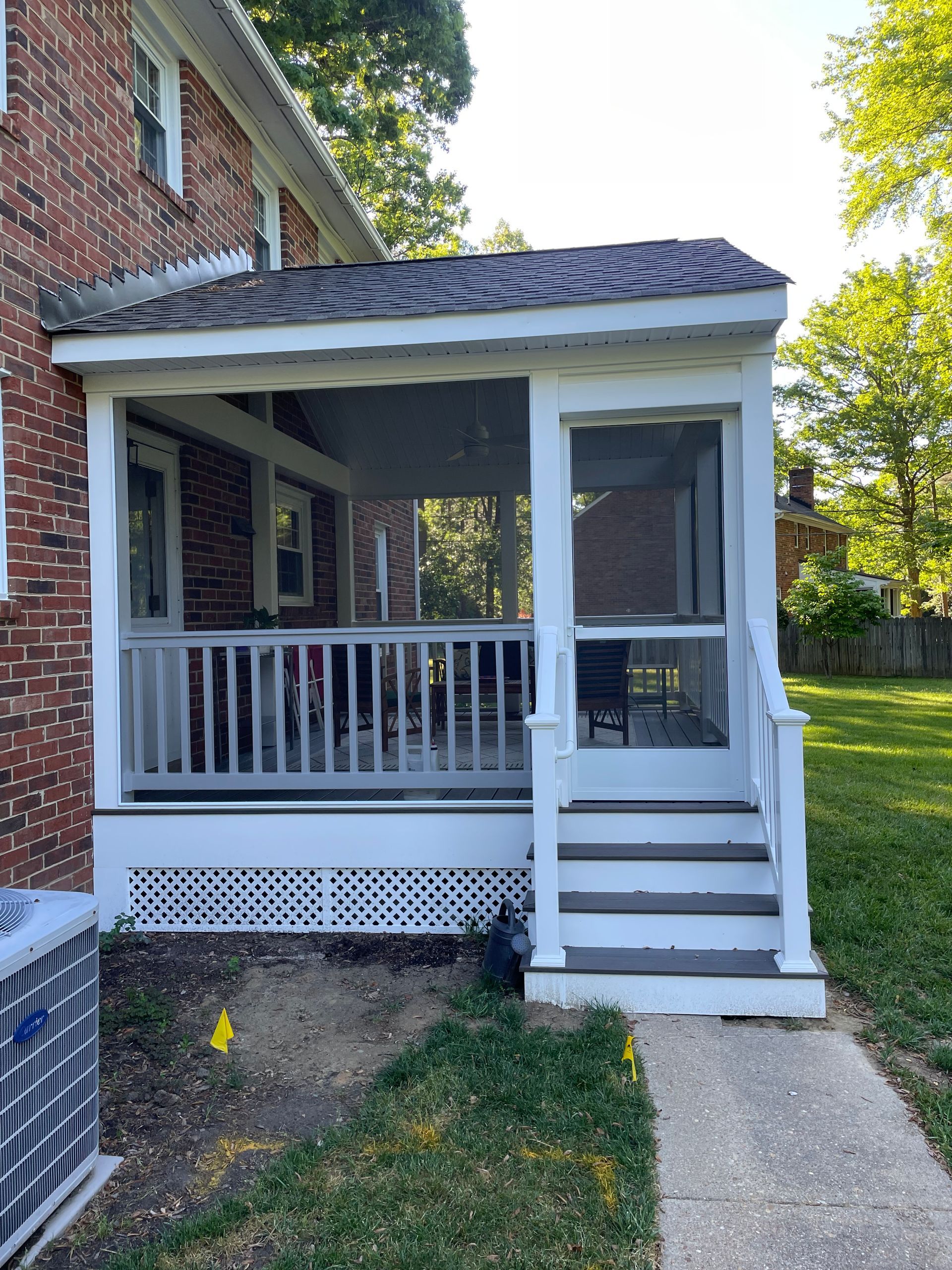 Brick house porch with white railings and steps leading to a screened entrance.