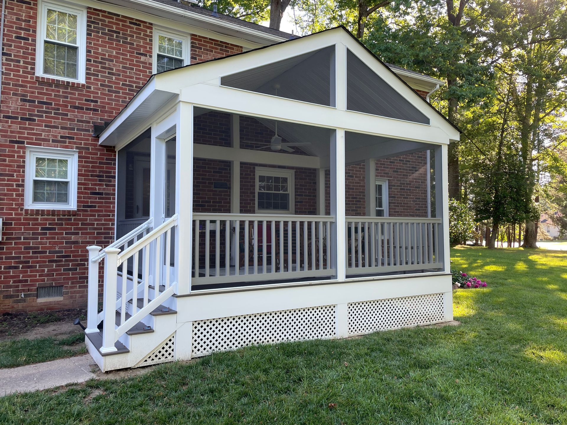 White screened porch with gabled roof attached to a red brick house, beside a grassy yard.
