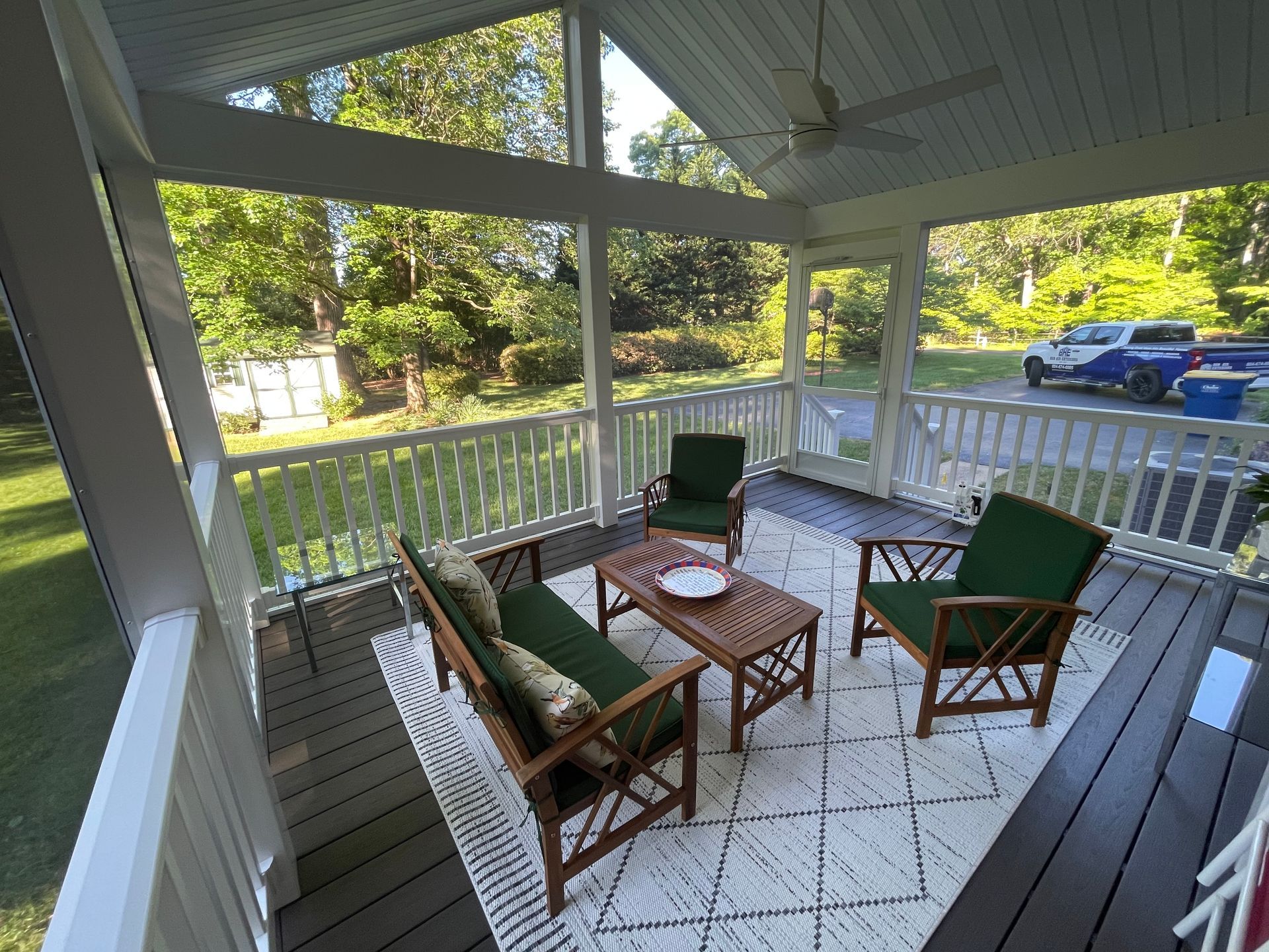 Covered porch with wicker chairs, small table, and a grill overlooking a yard and driveway