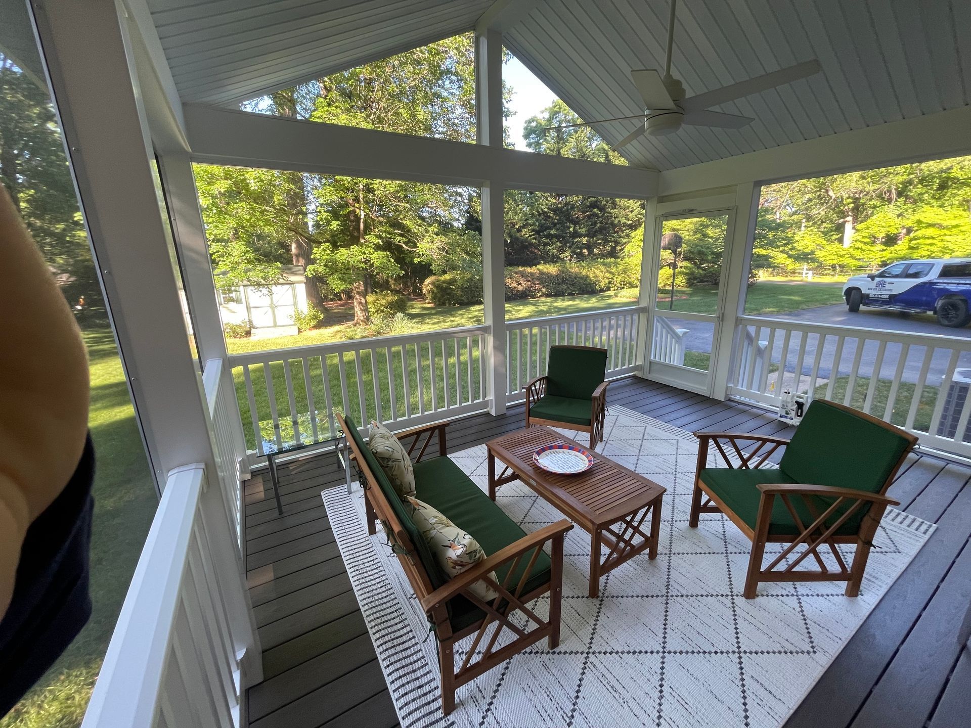 Covered porch seating area with wicker chairs, coffee table, and view of a yard and parked car