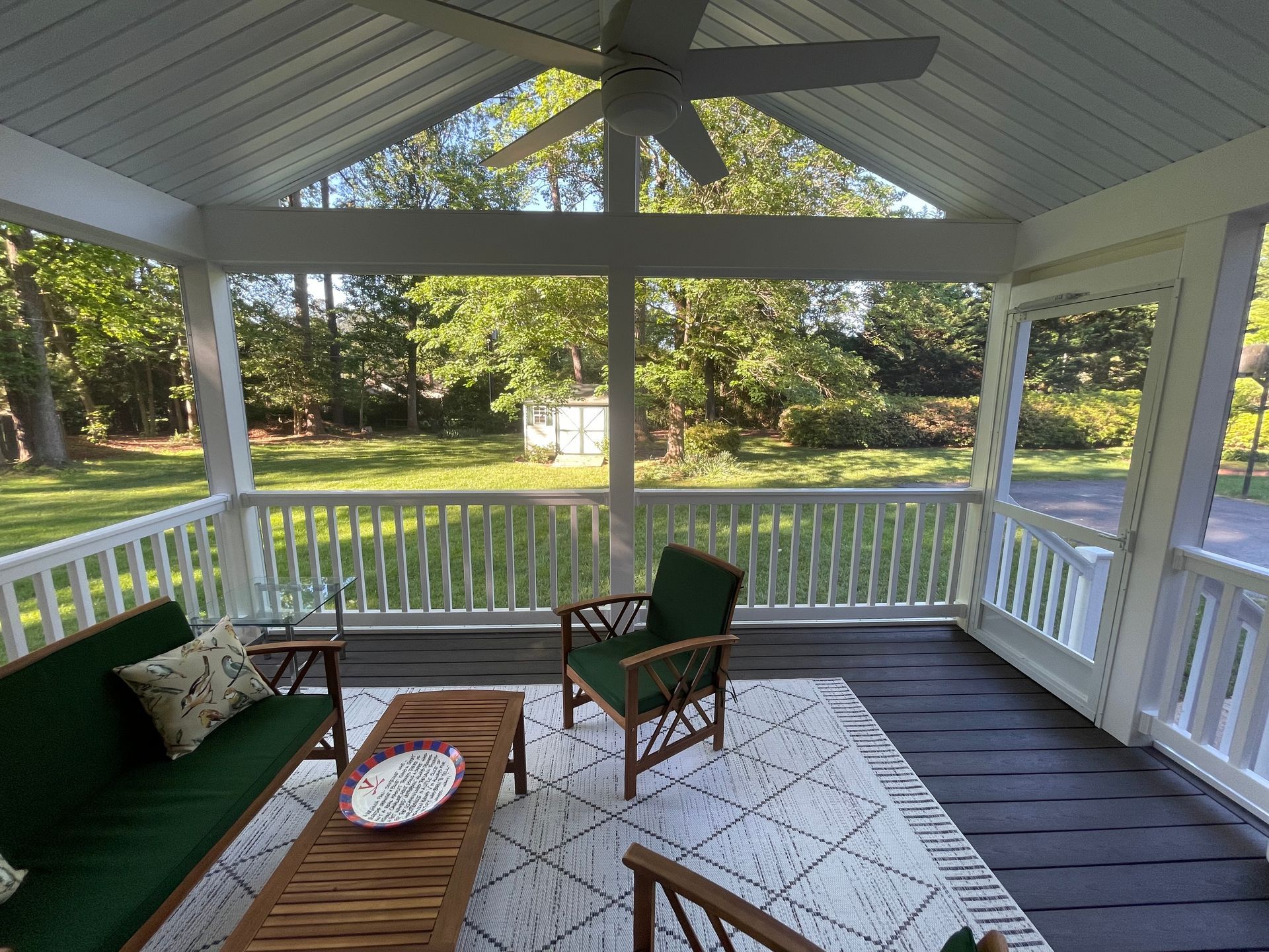 Covered porch with green sofa, wooden table, and chairs overlooking a grassy yard