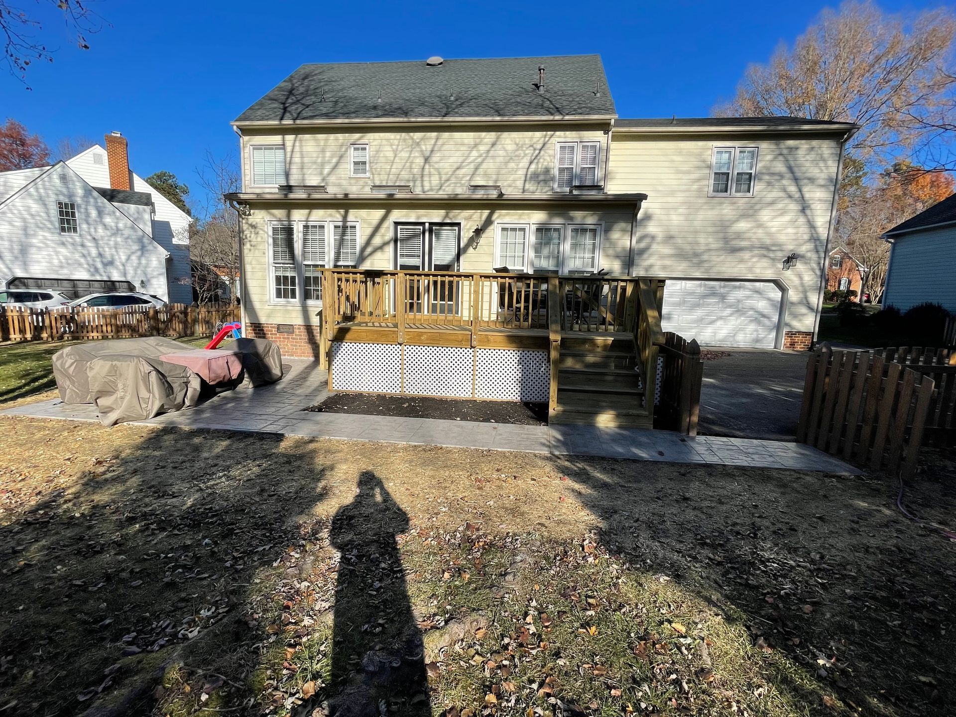 Backyard view of a house with a wooden deck and steps, winter yard, and blue sky