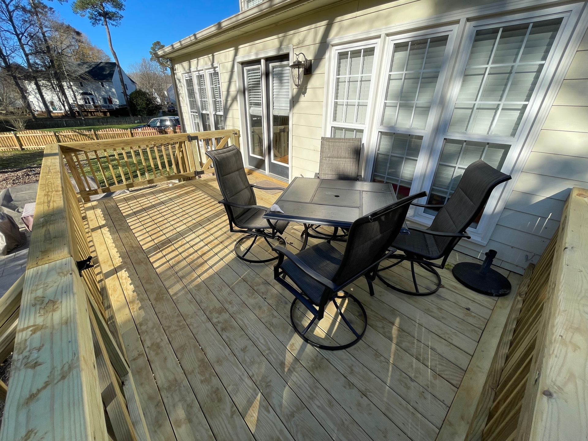 Wooden deck with patio table and chairs outside a house on a sunny day