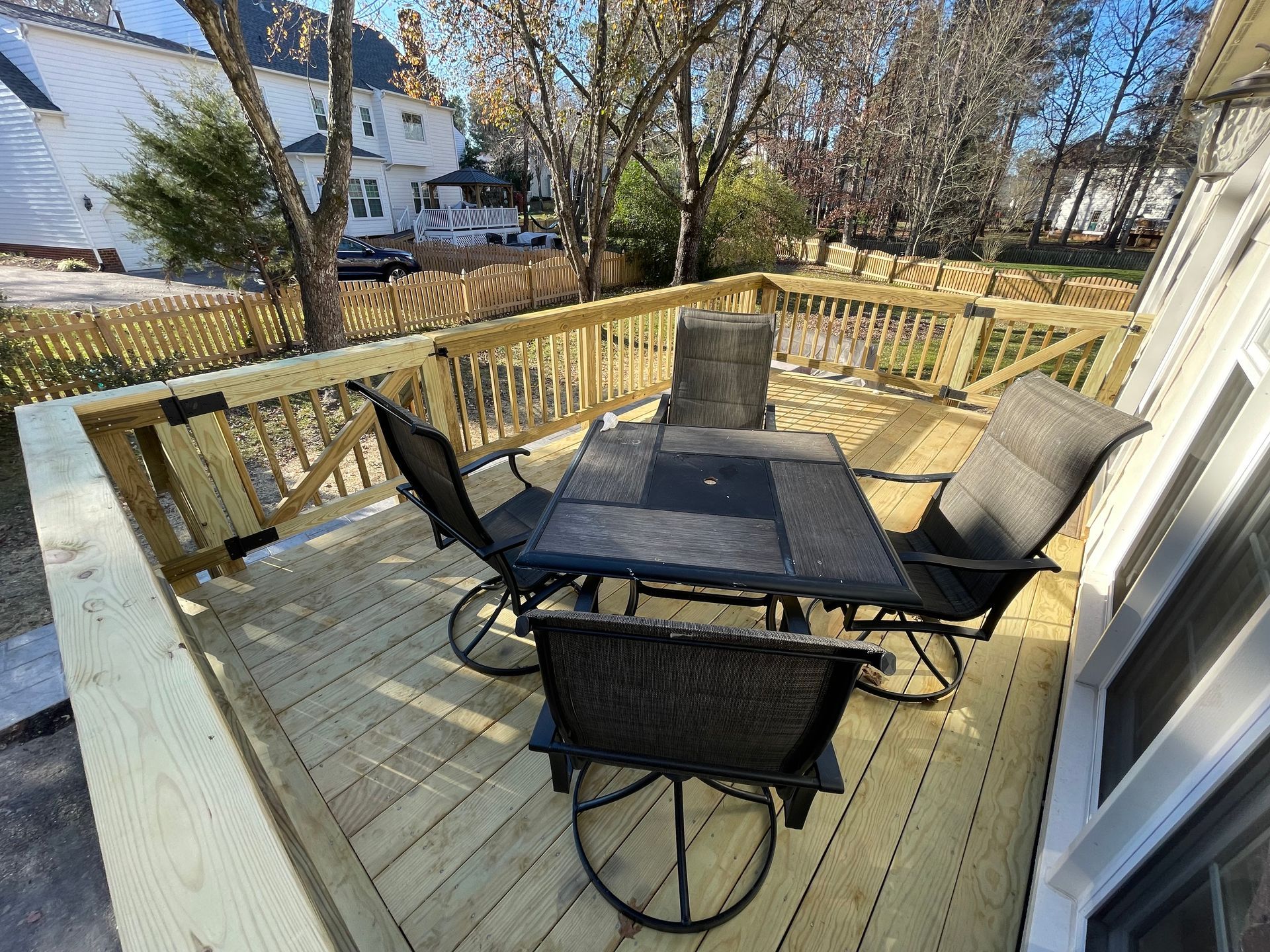 Wooden deck with patio table and four chairs beside a house, overlooking a snowy backyard