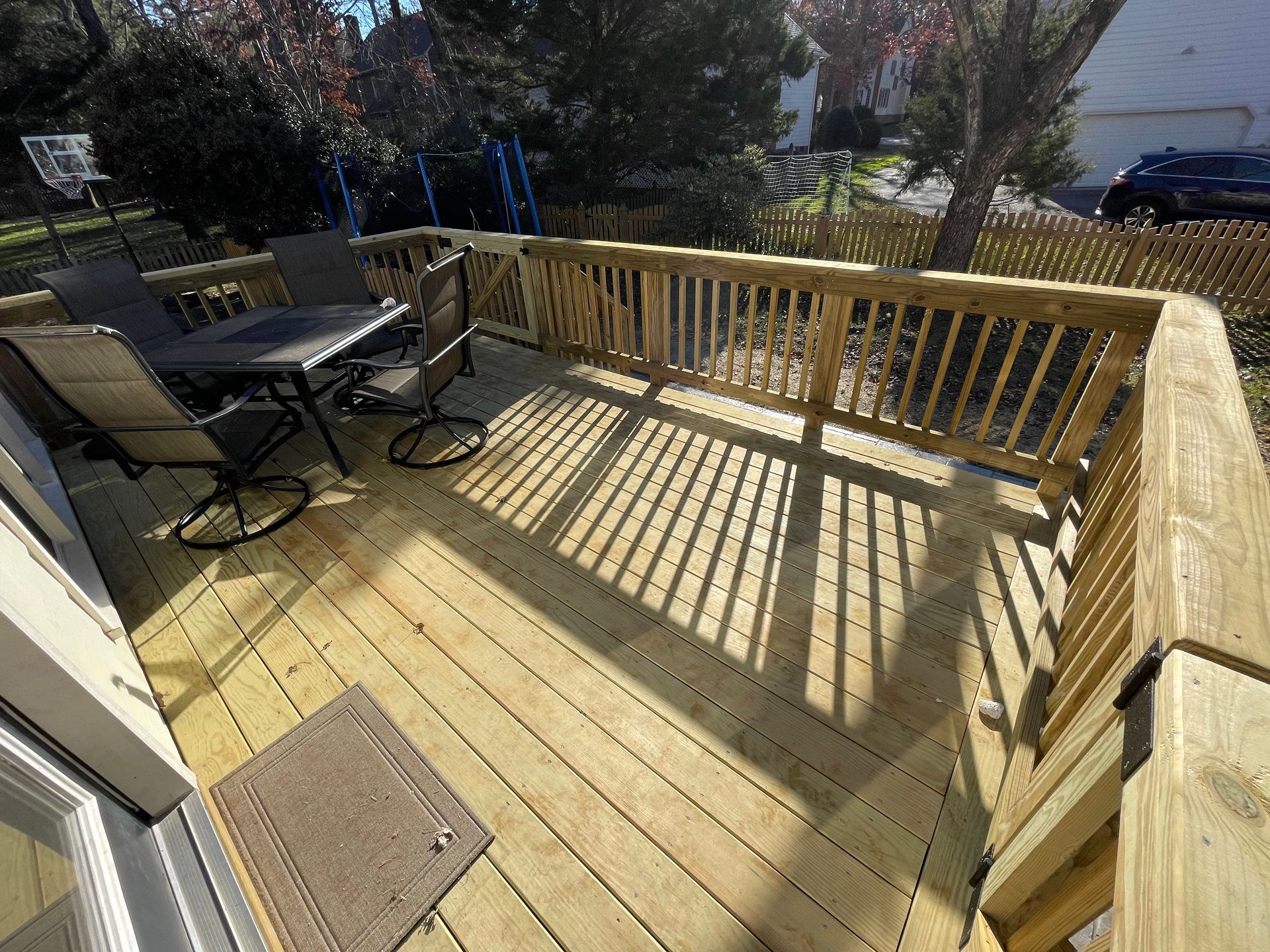 Sunlit wooden deck with railing, patio table and chairs, and long shadows across the floor.