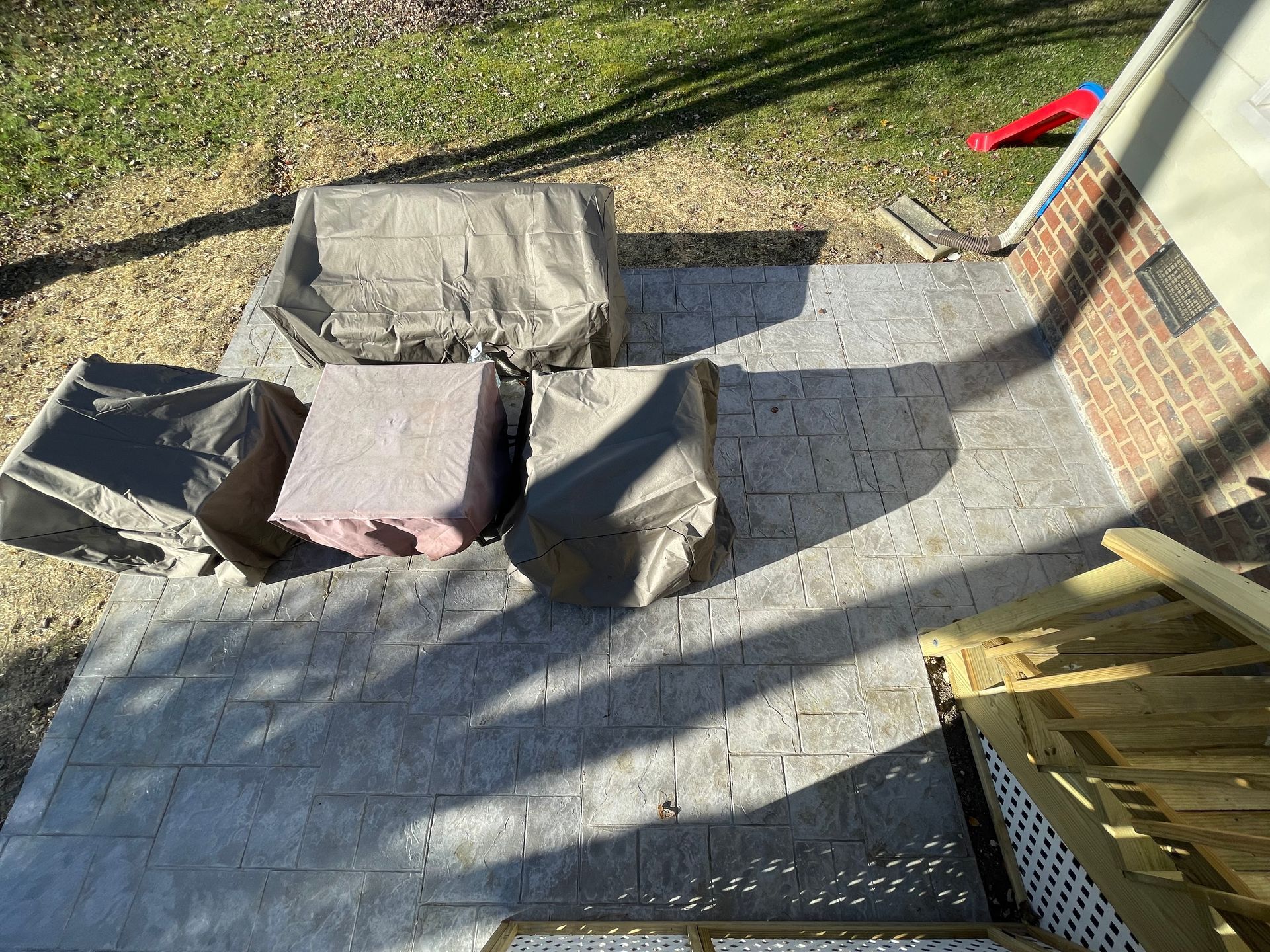 Outdoor deck with several covered patio chairs and a small wooden fence in sunlight.