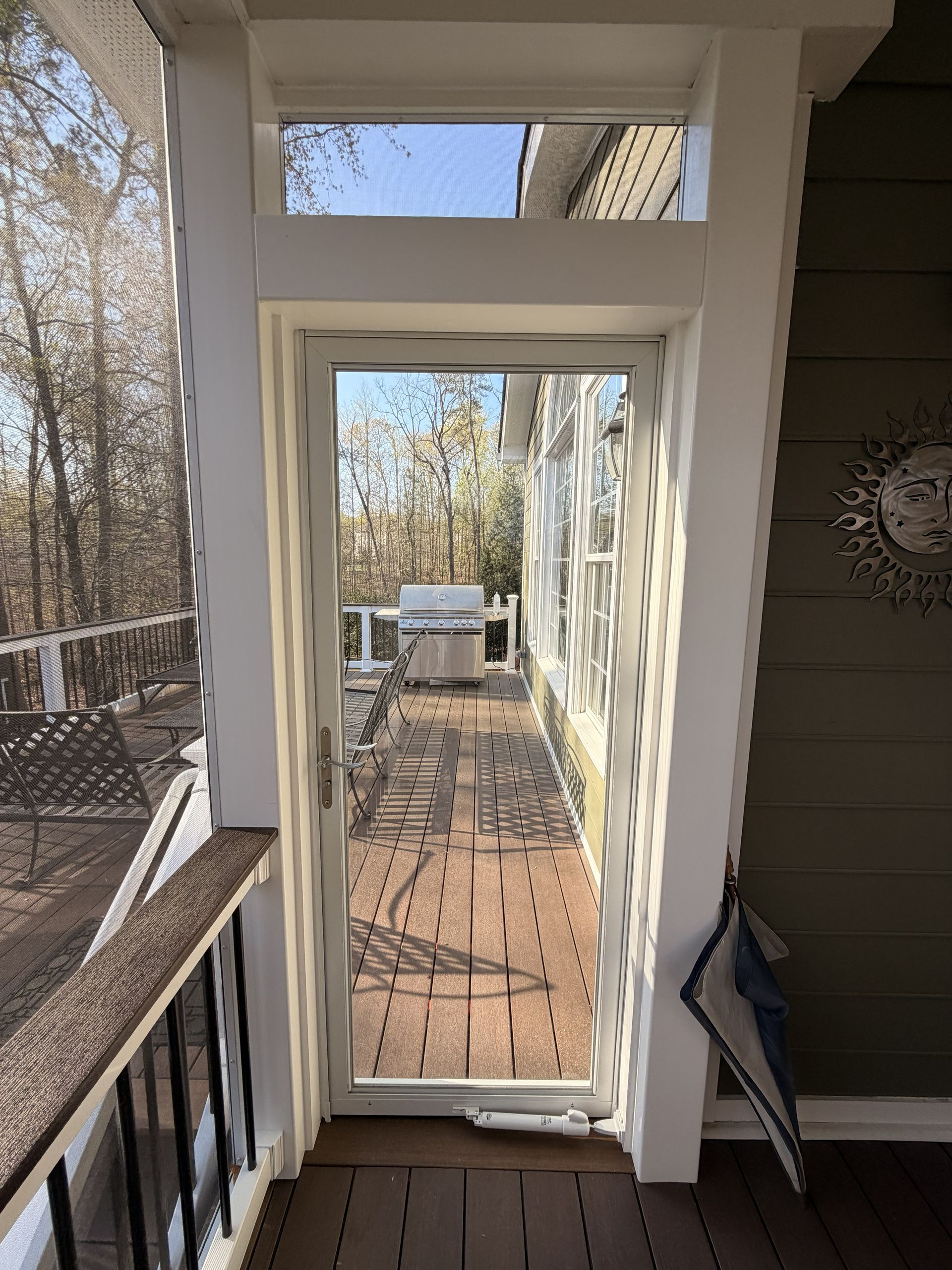 Balcony view through a white doorway to a wooden deck and trees beyond