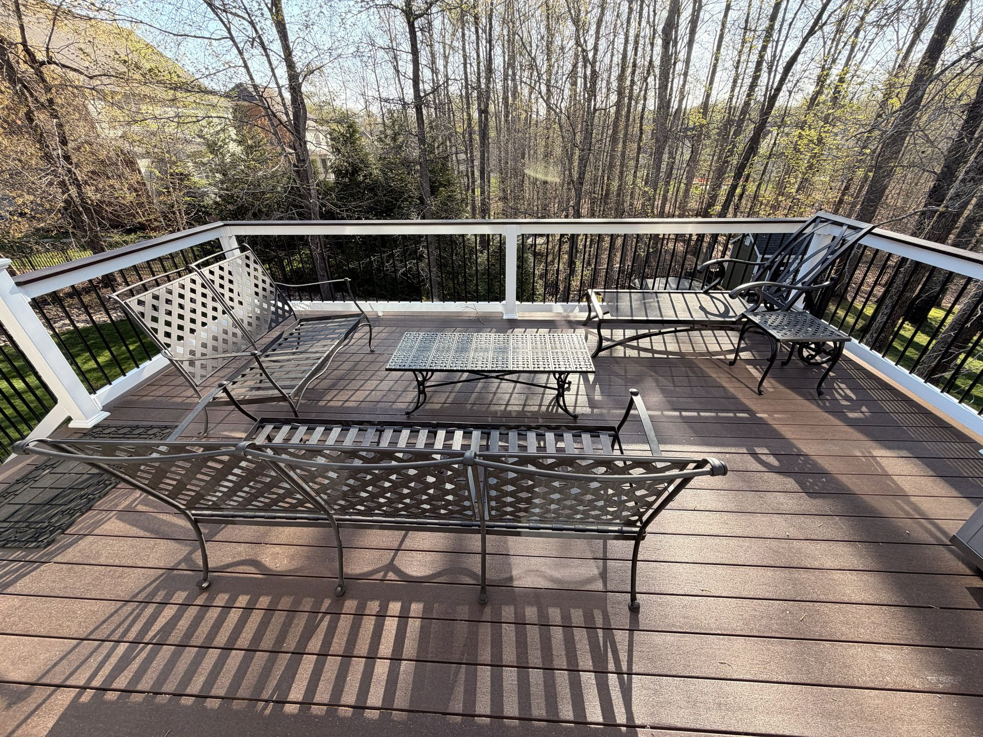 Outdoor wooden deck with black metal tables and chairs, white railing, and leafless trees beyond