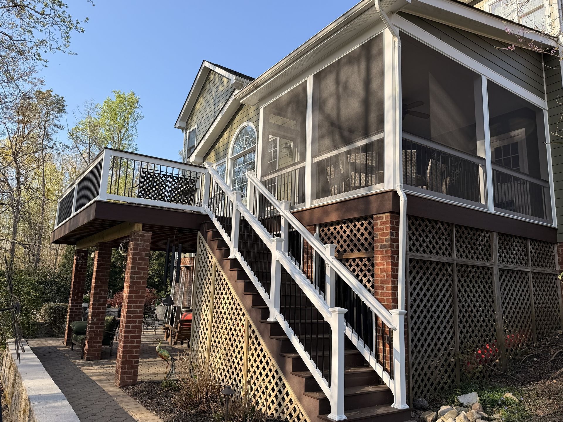 Raised house with screened porch, exterior staircase, and wooden deck in a wooded setting