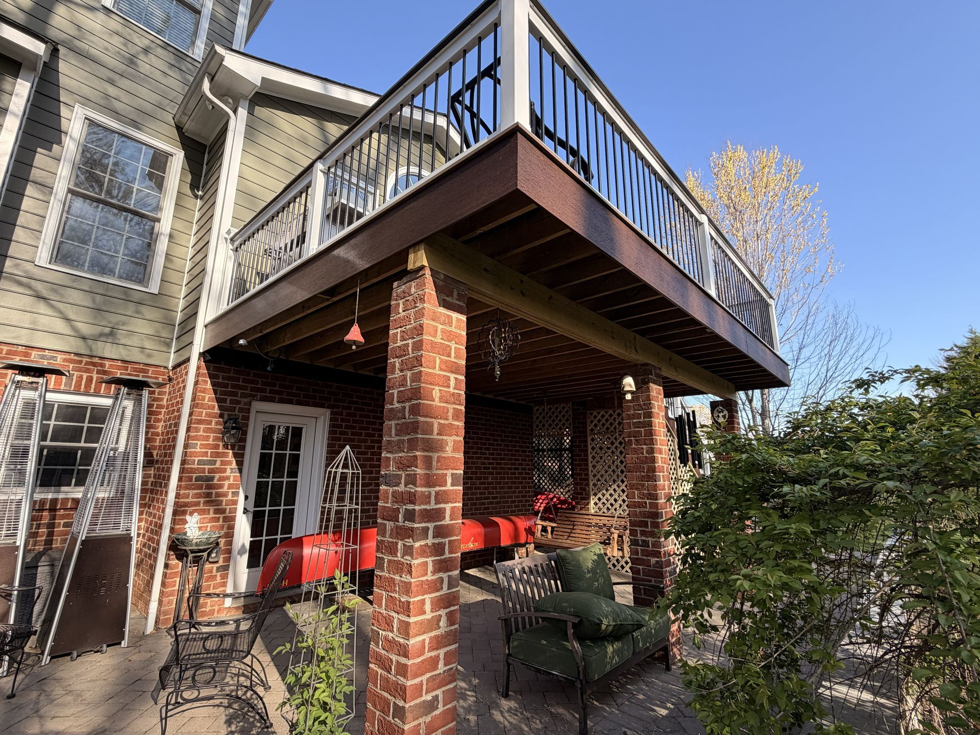 Brick house patio with red chairs, brick columns, and an upper deck on a sunny day