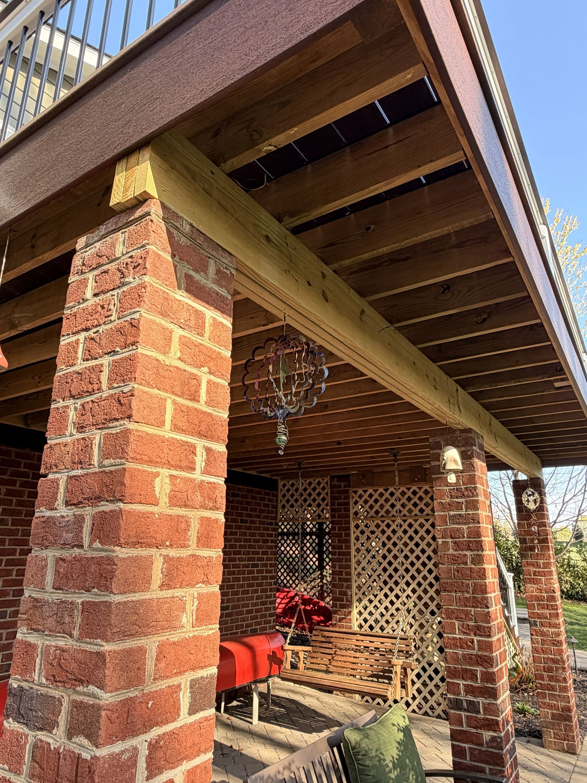Brick porch with wooden beams, red chair, and hanging chandelier under a sloped roof