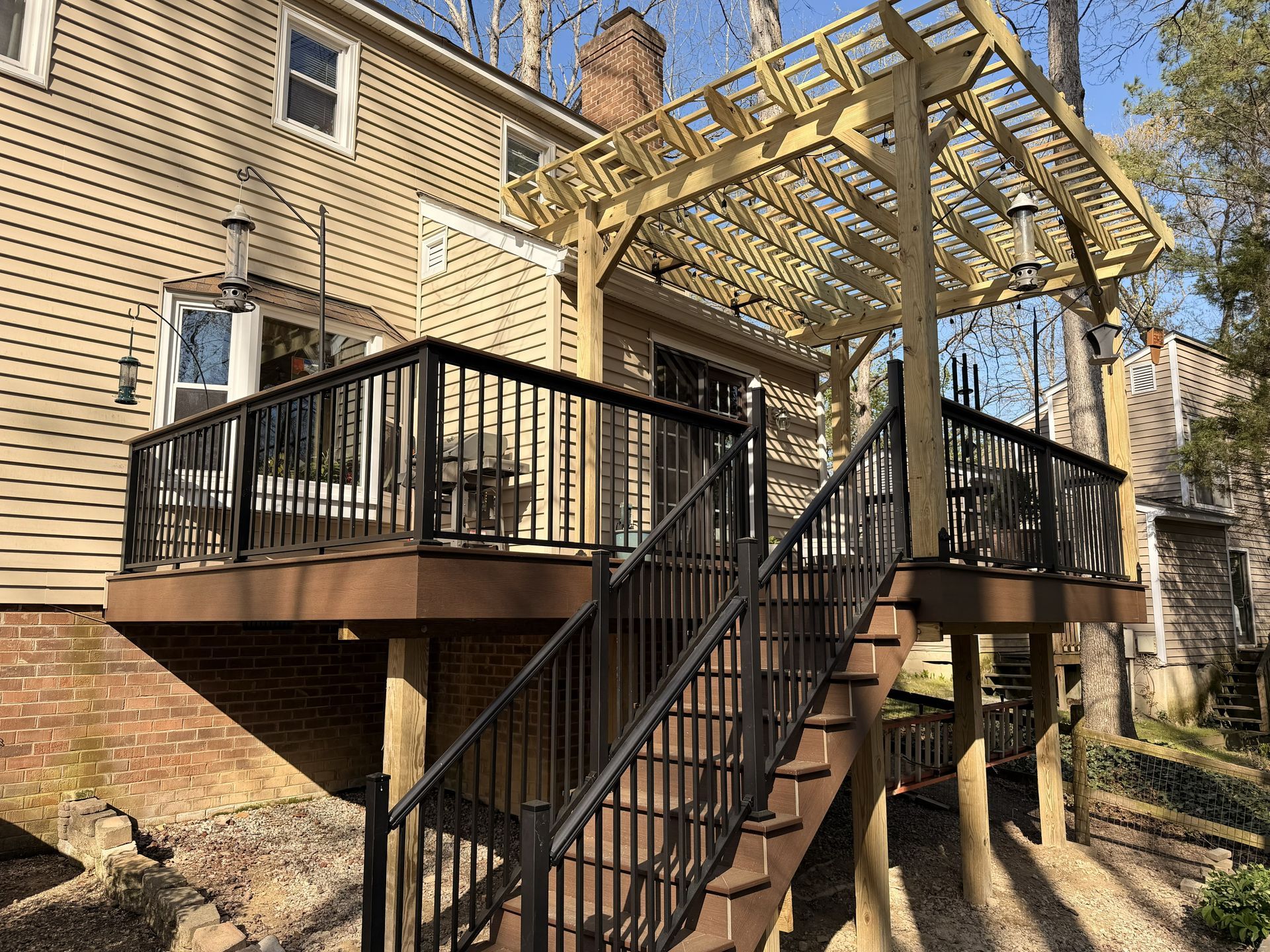 Backyard deck with black railings and pergola attached to a beige house, viewed from below