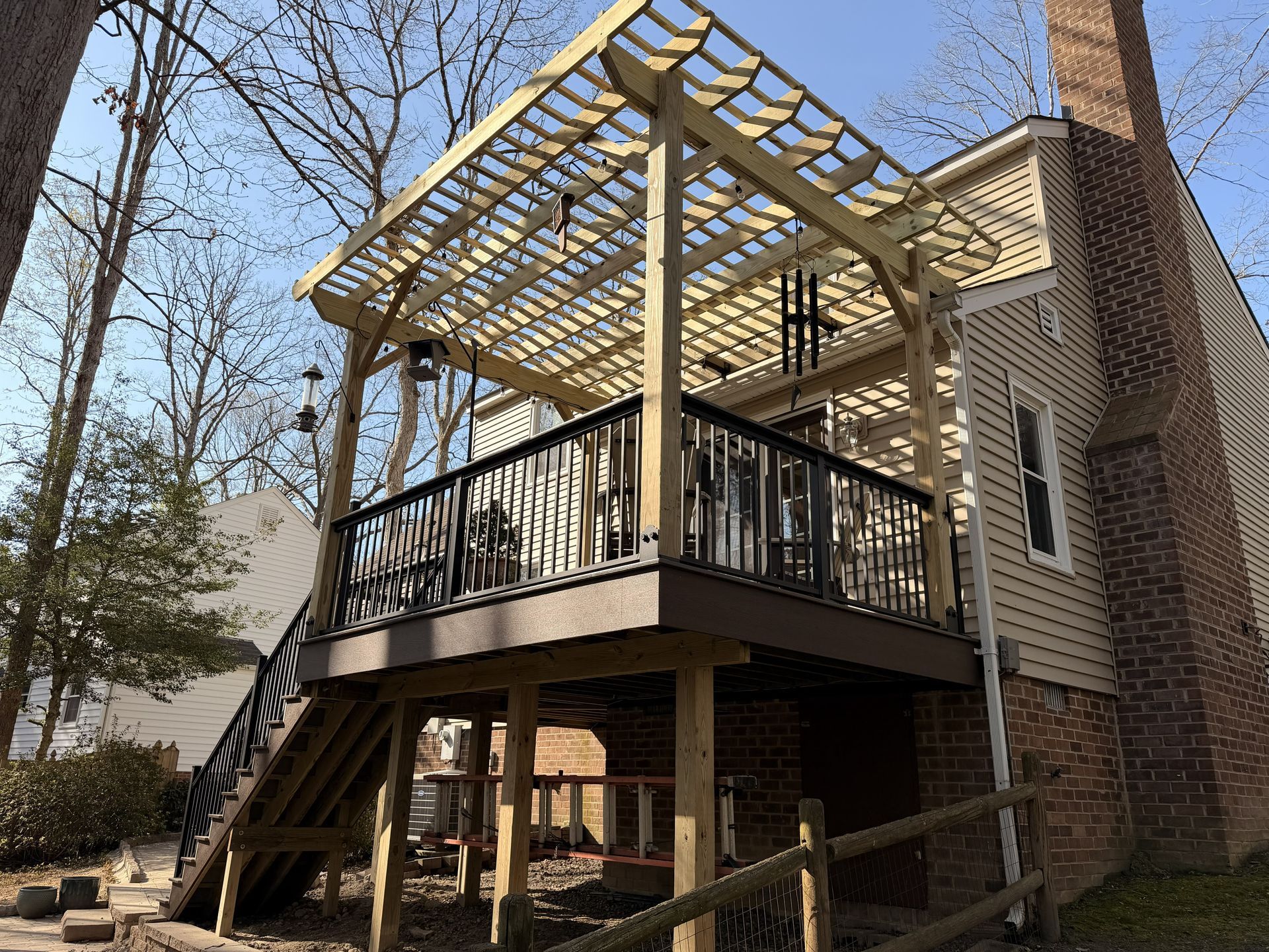 Back porch with black railings, stairs, and a wooden pergola attached to a brick house