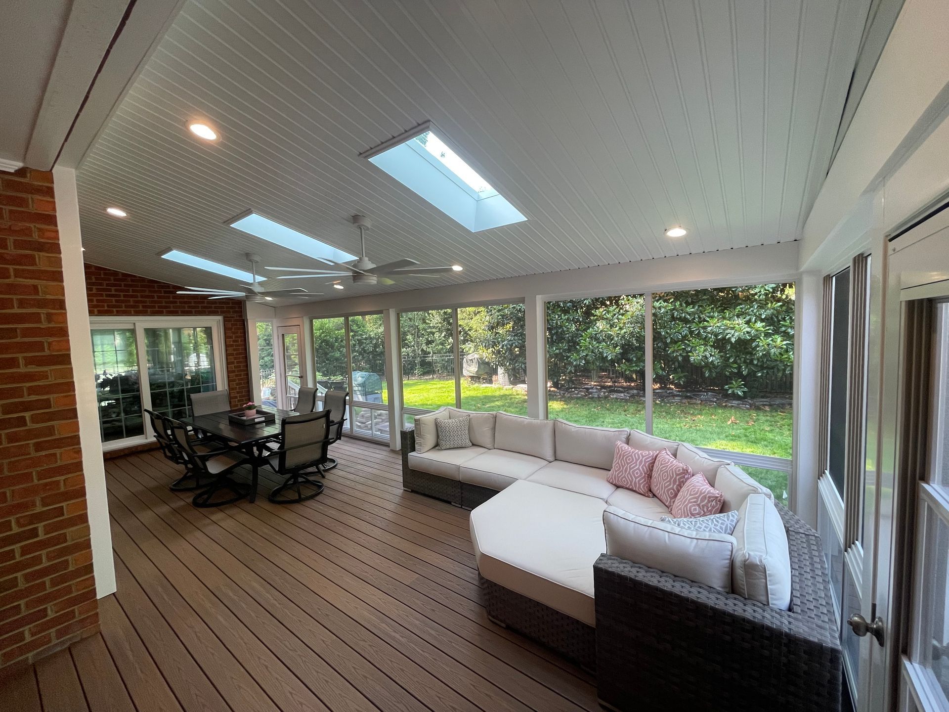 Covered patio with wicker seating, white chaise lounge, and dining table overlooking a lush green yard