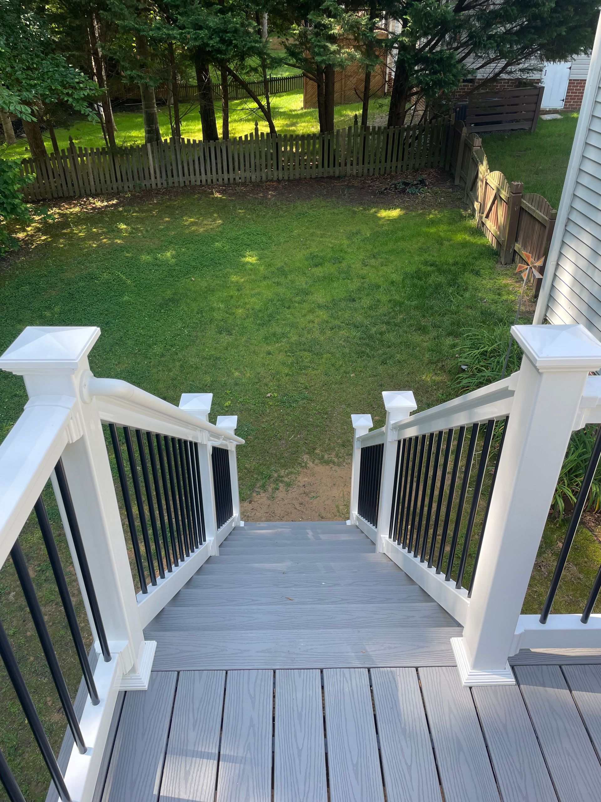 Wooden porch stairs leading down to a grassy backyard with a fenced tree-lined edge