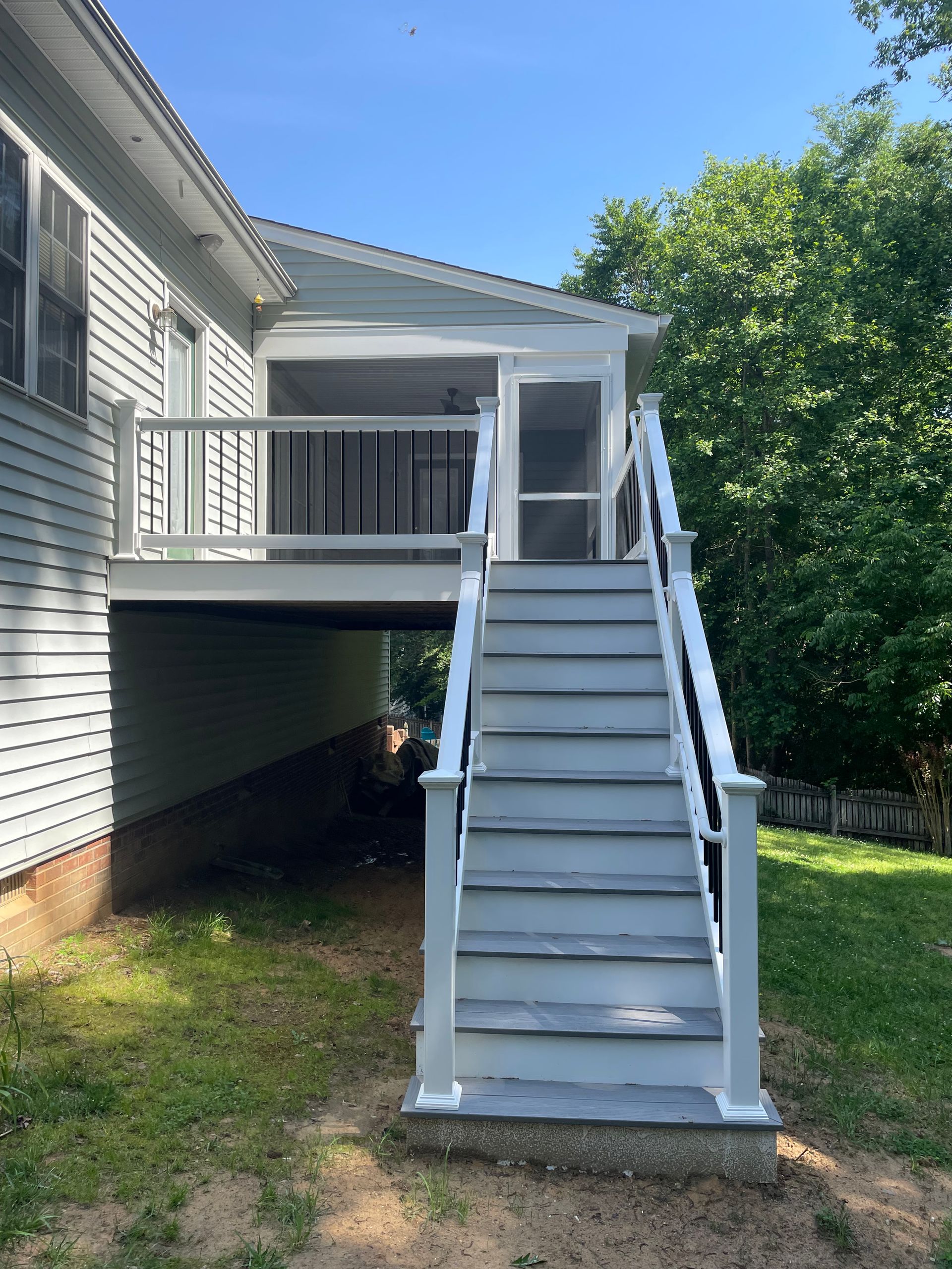 White exterior staircase leading to an elevated deck on a house, with siding and trees in the background.